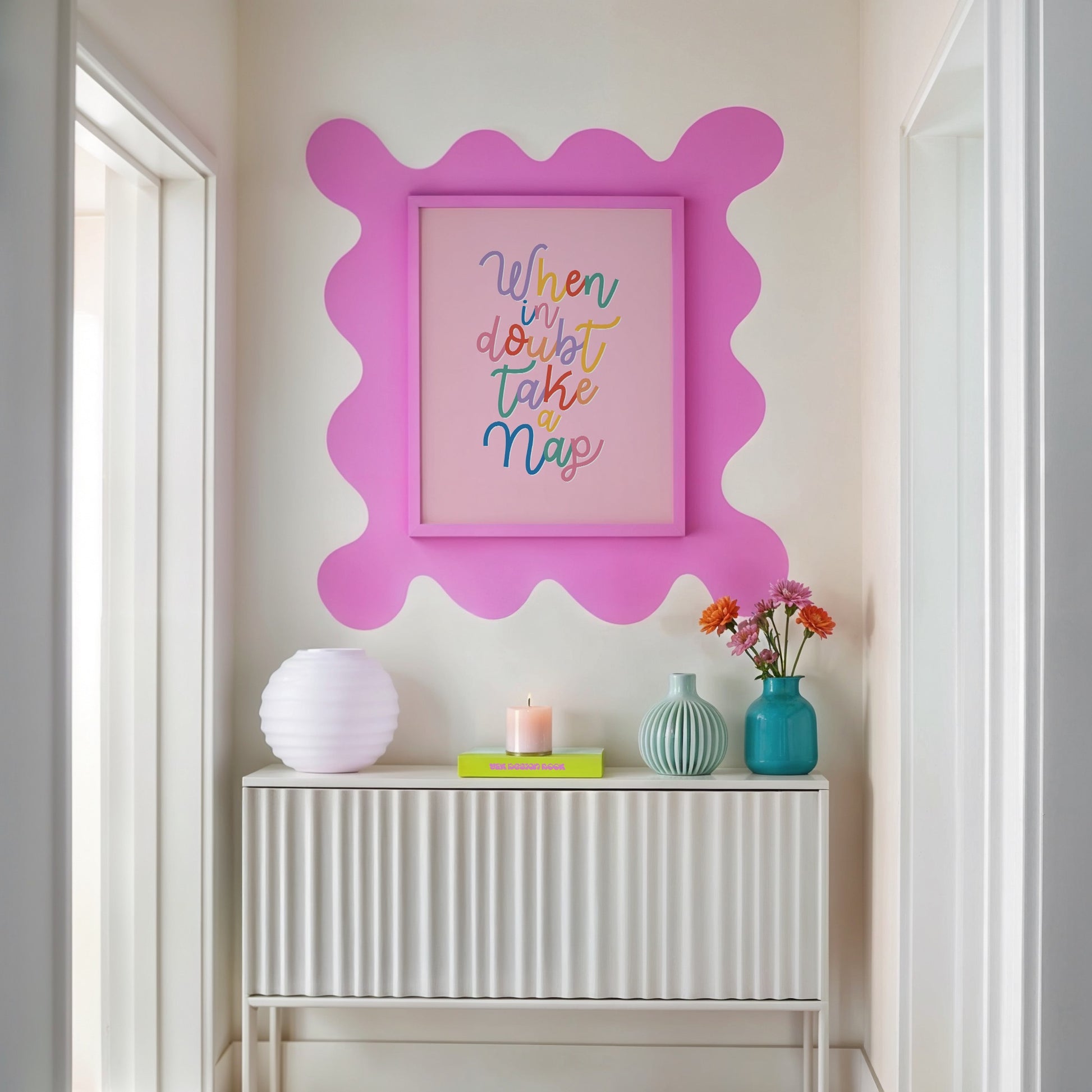 Decorative wall art with a pink frame and colourful text on a white wall above a console table.