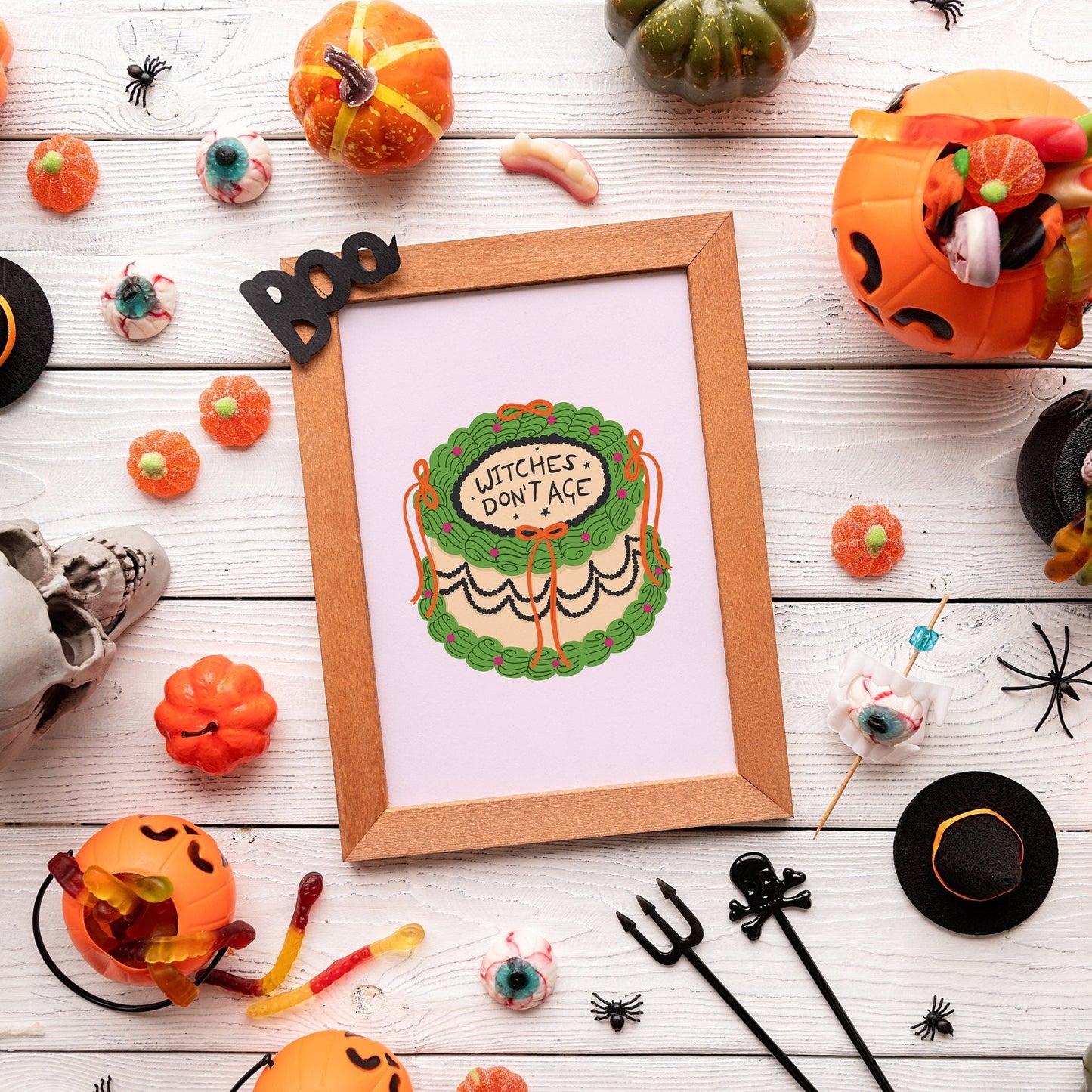 An illustration print, of a cake, in Halloween themed colours, with the words 'Witches Don't Age' on the top of the cake.