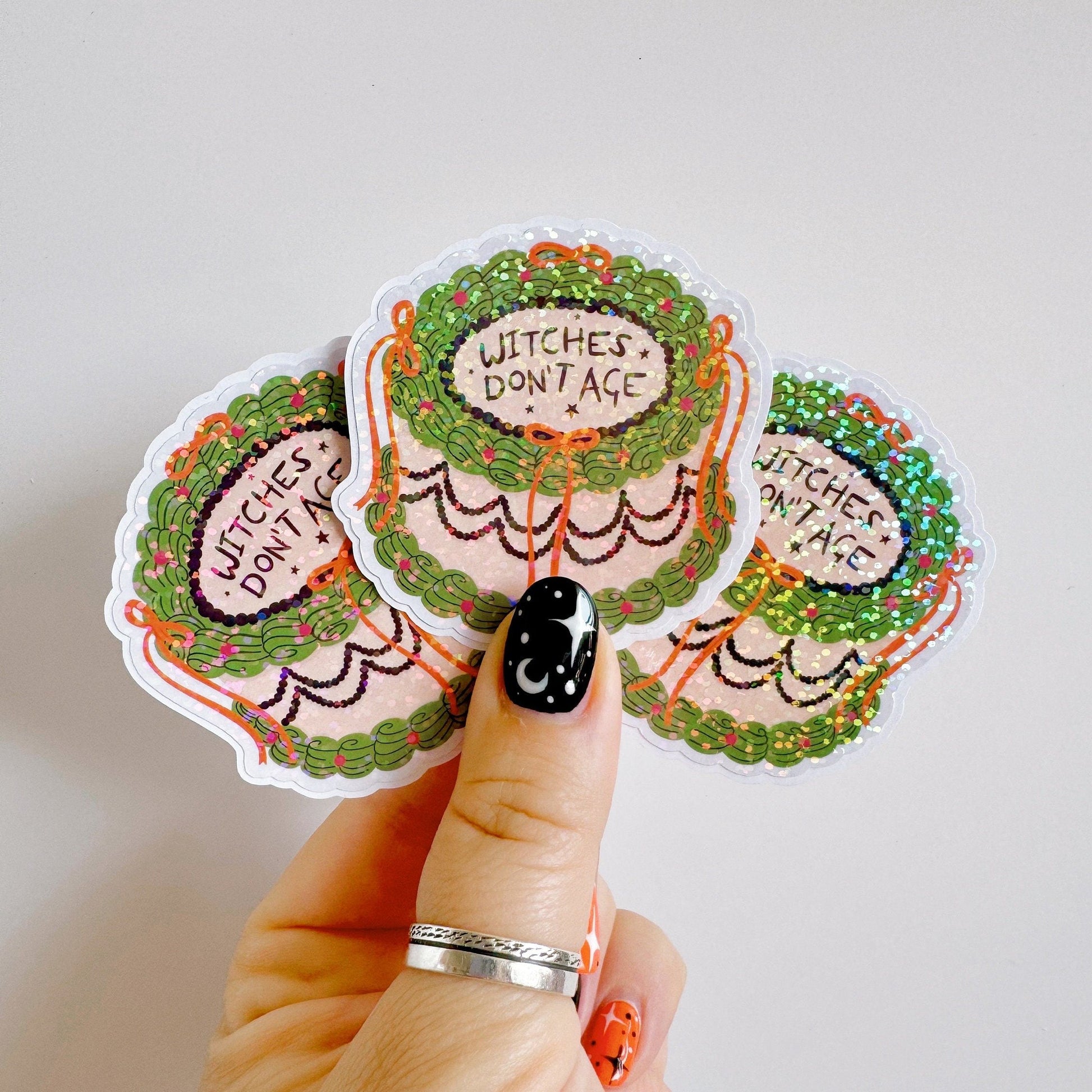 A holographic sticker, of a decorative cake with the words witches don't age on the top. The sticker has an easy peel lip.