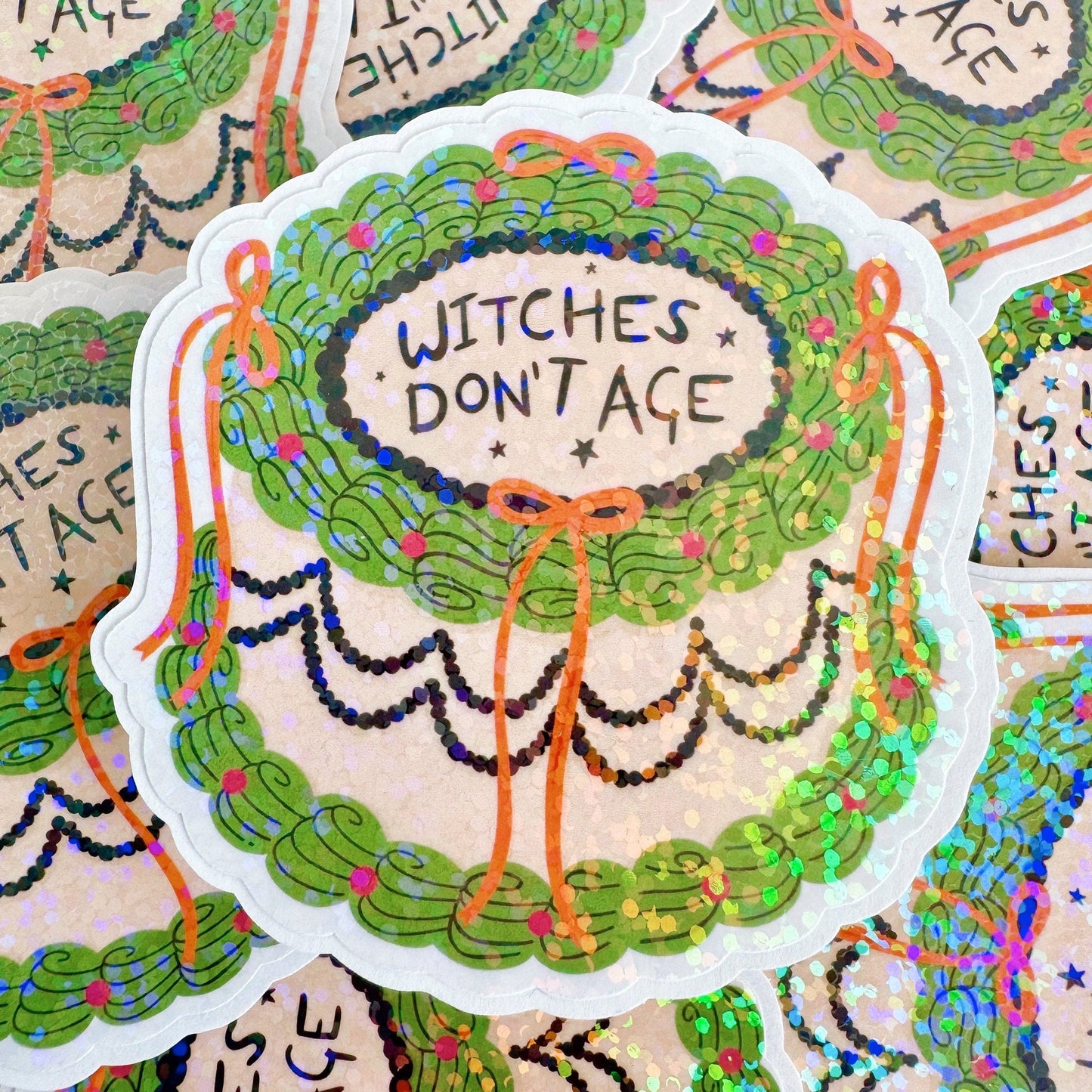 A holographic sticker, of a decorative cake with the words witches don't age on the top. The sticker has an easy peel lip.