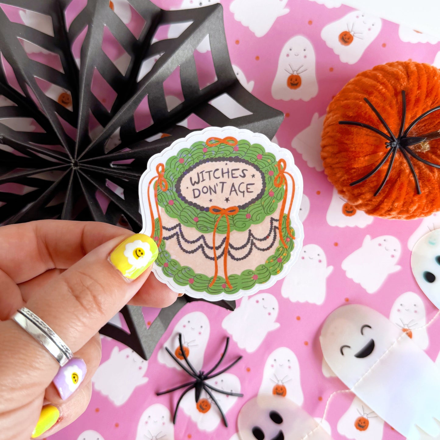 A holographic sticker, of a decorative cake with the words witches don't age on the top. The sticker has an easy peel lip.