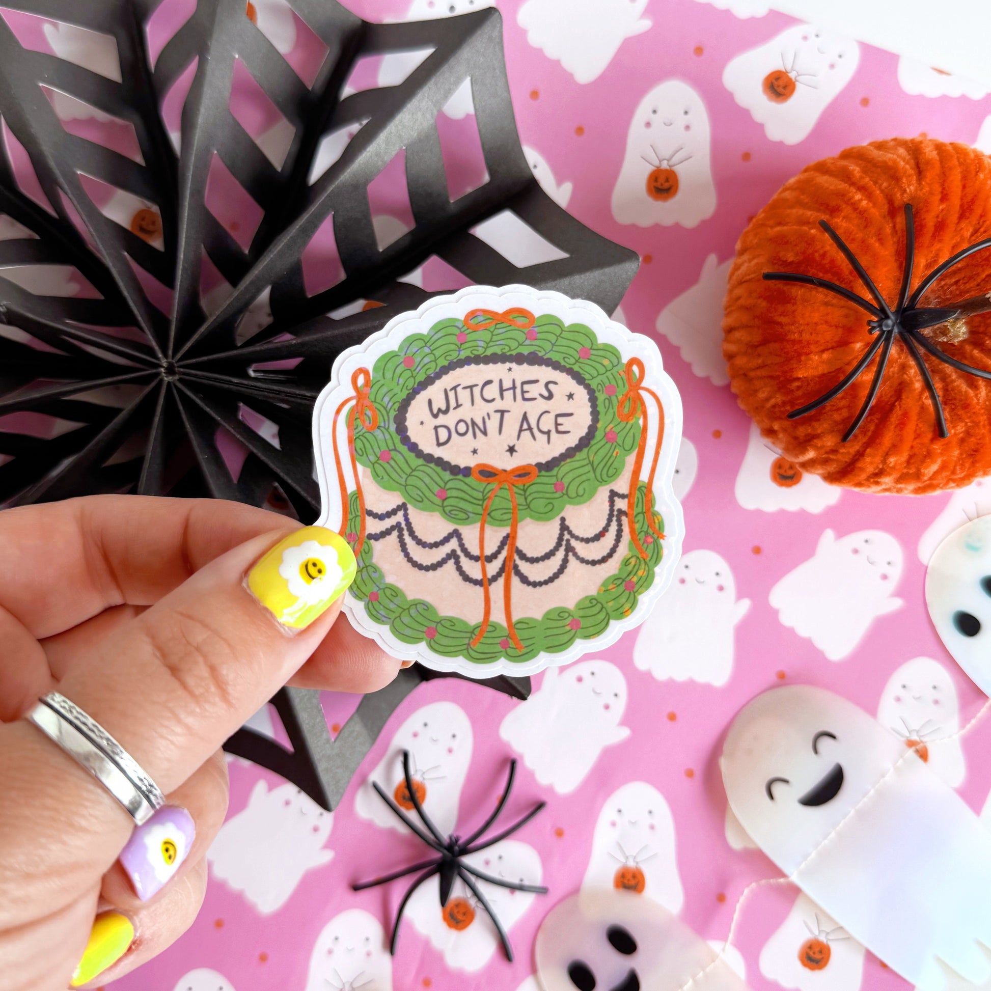 A holographic sticker, of a decorative cake with the words witches don't age on the top. The sticker has an easy peel lip.