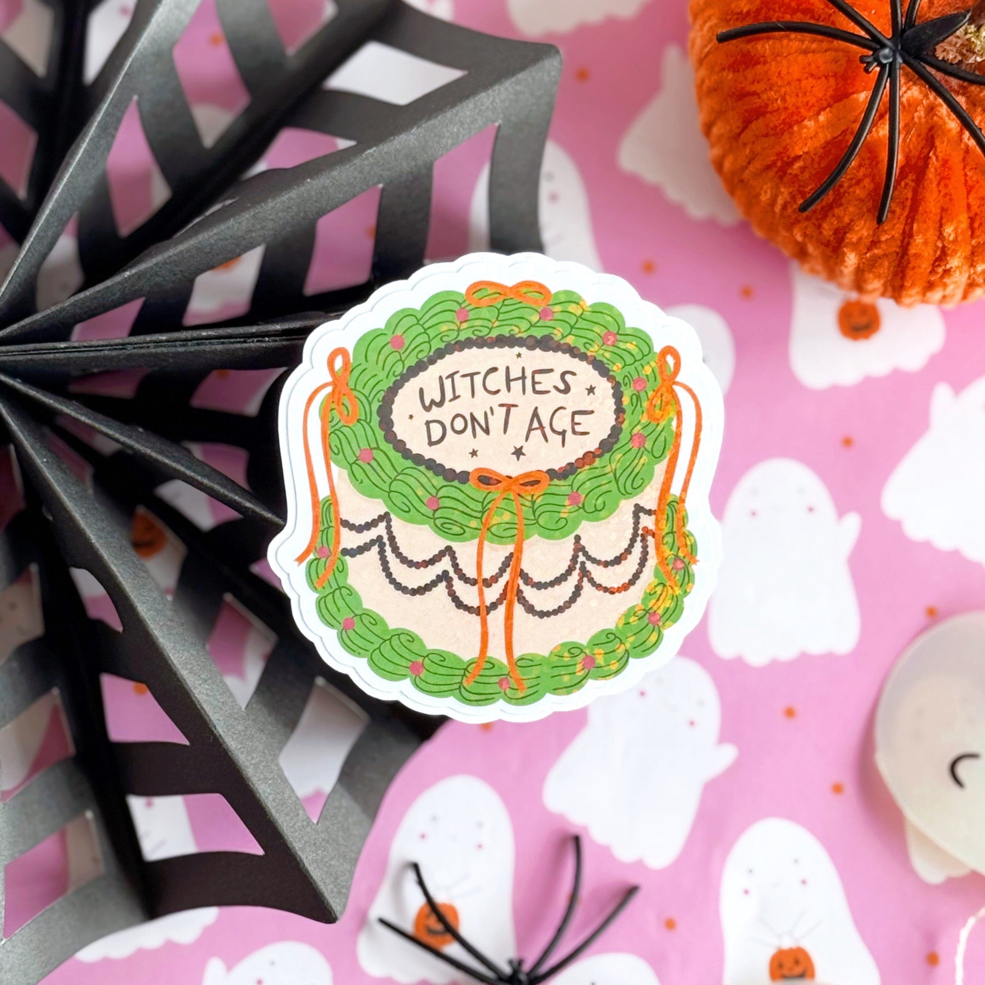 A holographic sticker, of a decorative cake with the words witches don't age on the top. The sticker has an easy peel lip.