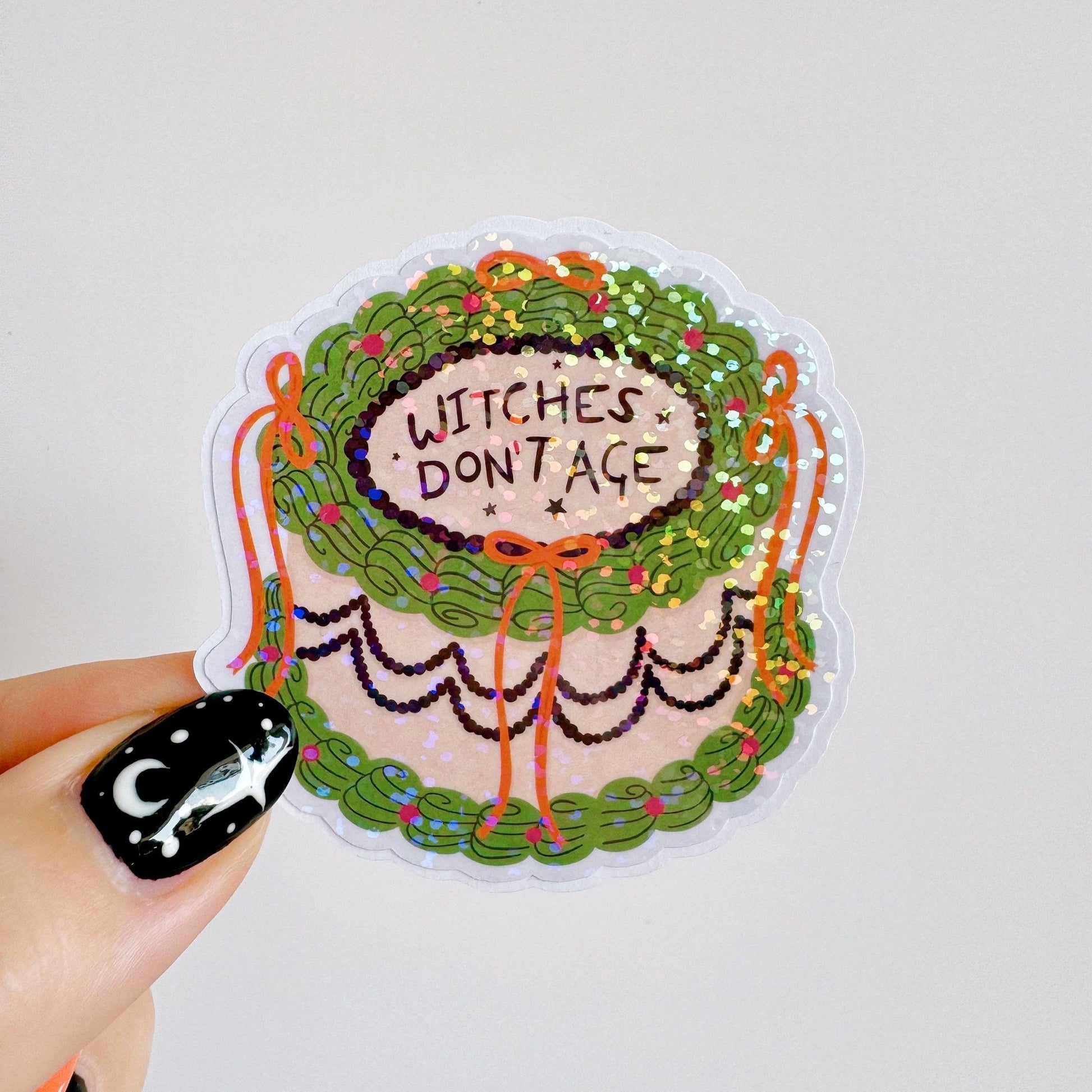 A holographic sticker, of a decorative cake with the words witches don't age on the top. The sticker has an easy peel lip.