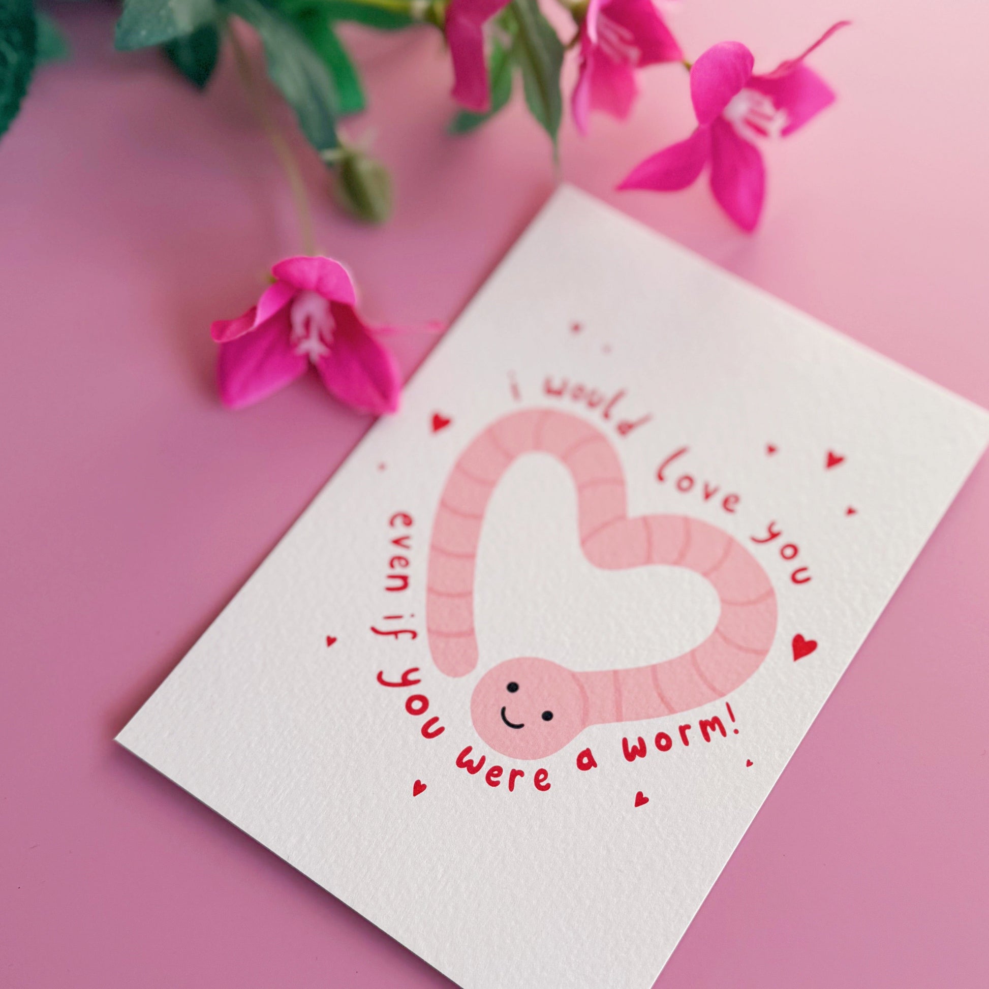A textured postcard with an illustration of a worm in the shape of a heart, with the words 'I would love you even if you were a worm!' around the illustration.