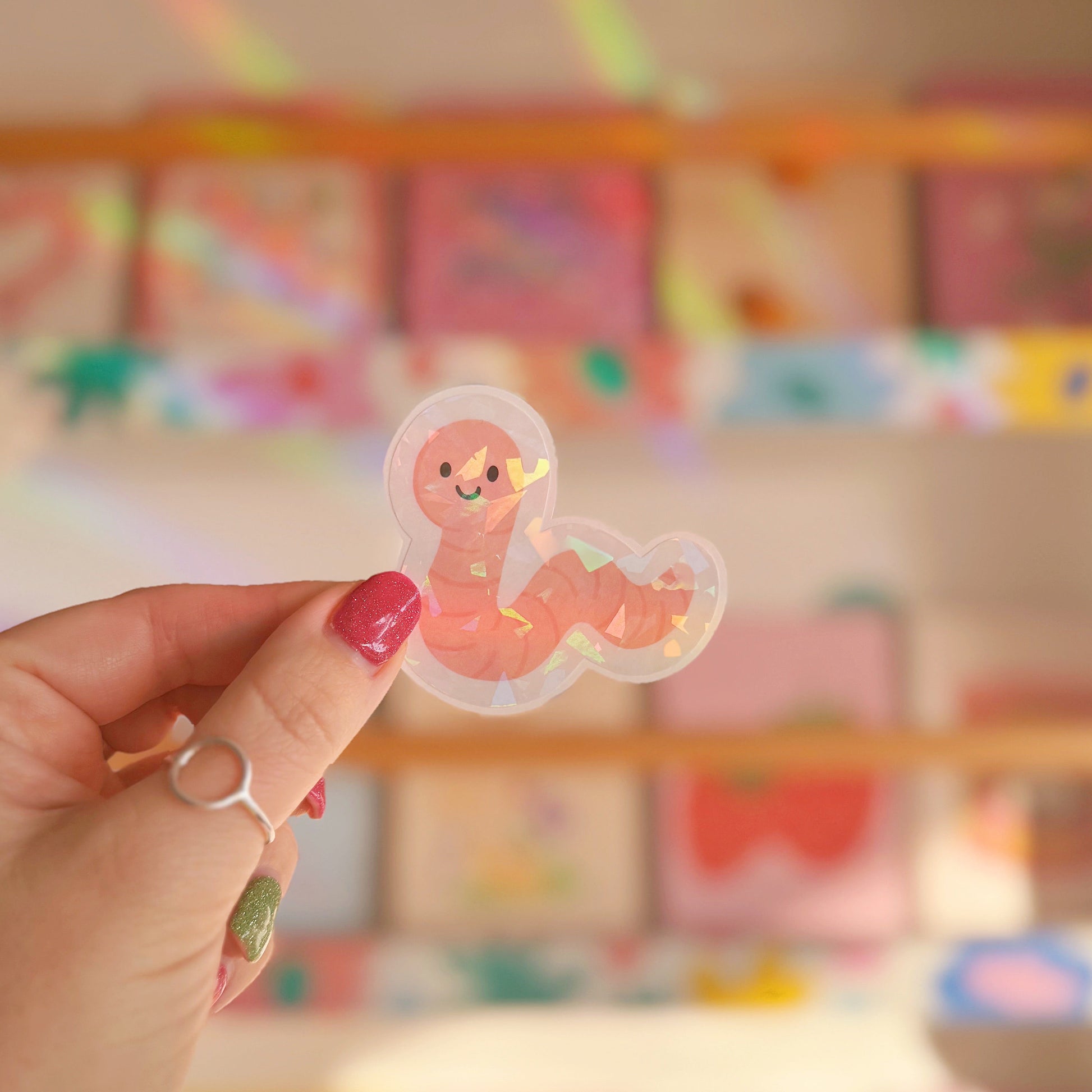 A holographic sticker featuring an illustration of a smiling worm.