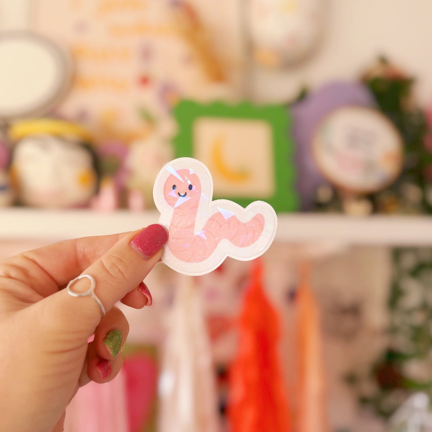 A holographic sticker featuring an illustration of a smiling worm.