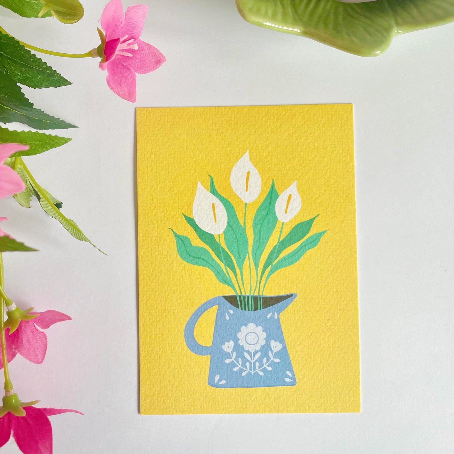 A yellow textured postcard with an illustration of a blue vase with white calla Lillies in it. 