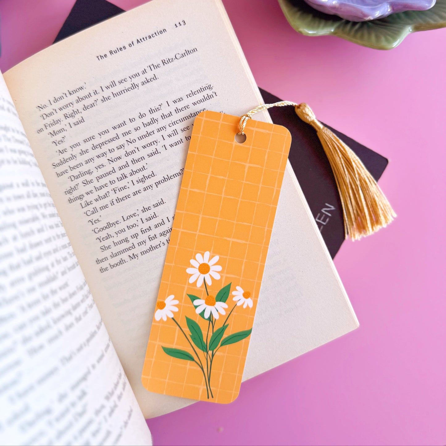 A yellow bookmark with a coordinating tassel, featuring an illustration of a bunch of daisies.