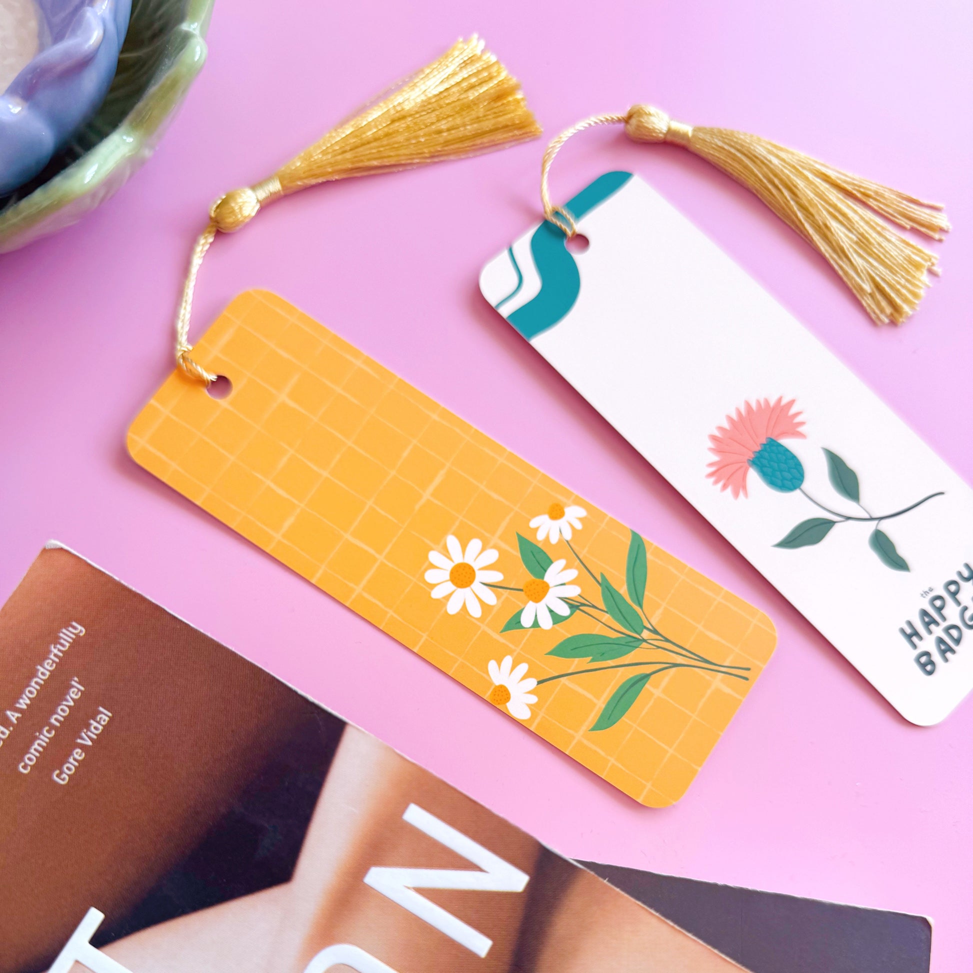 A yellow bookmark with a coordinating tassel, featuring an illustration of a bunch of daisies.