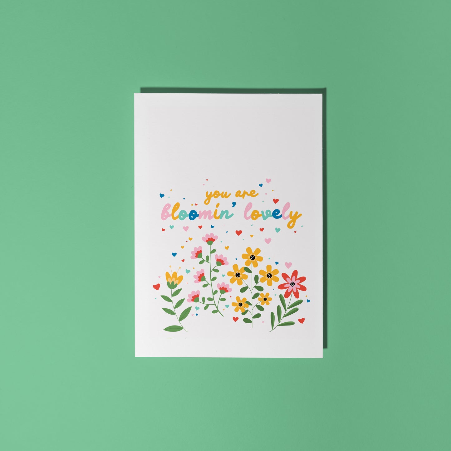 A white card, with a floral illustration scene at the bottom and the words 'you are bloomin' lovely' in colourful handwriting above the flowers.