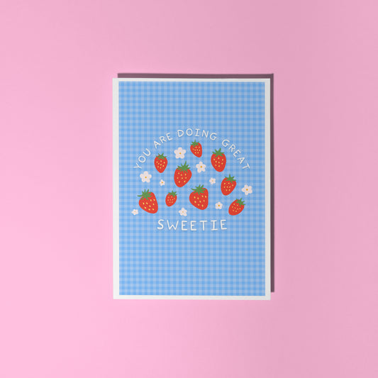 Card with strawberry design and text that reads 'you are doing great sweetie' on a blue gingham background