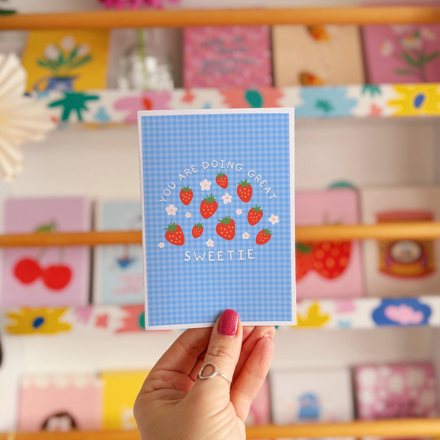 Card with strawberry design and text that reads 'you are doing great sweetie' on a blue gingham background