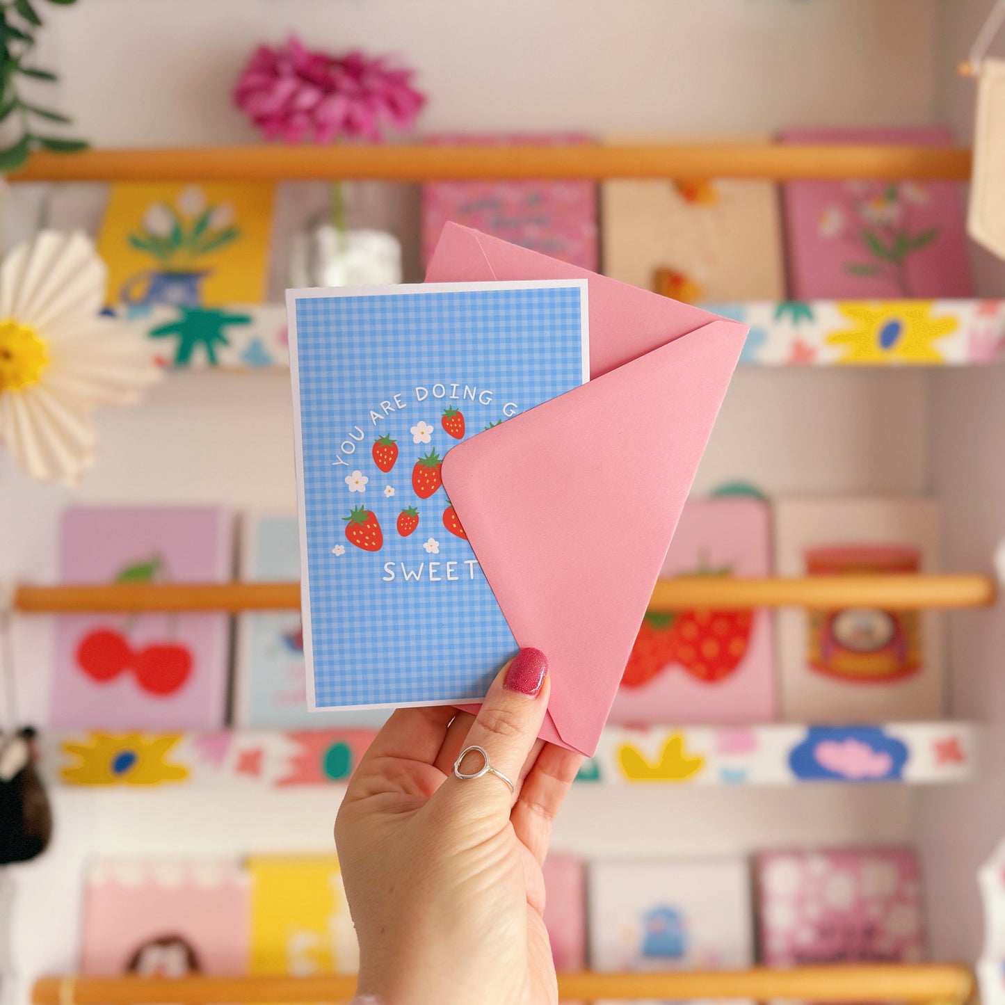 Card with strawberry design and text that reads 'you are doing great sweetie' on a blue gingham background