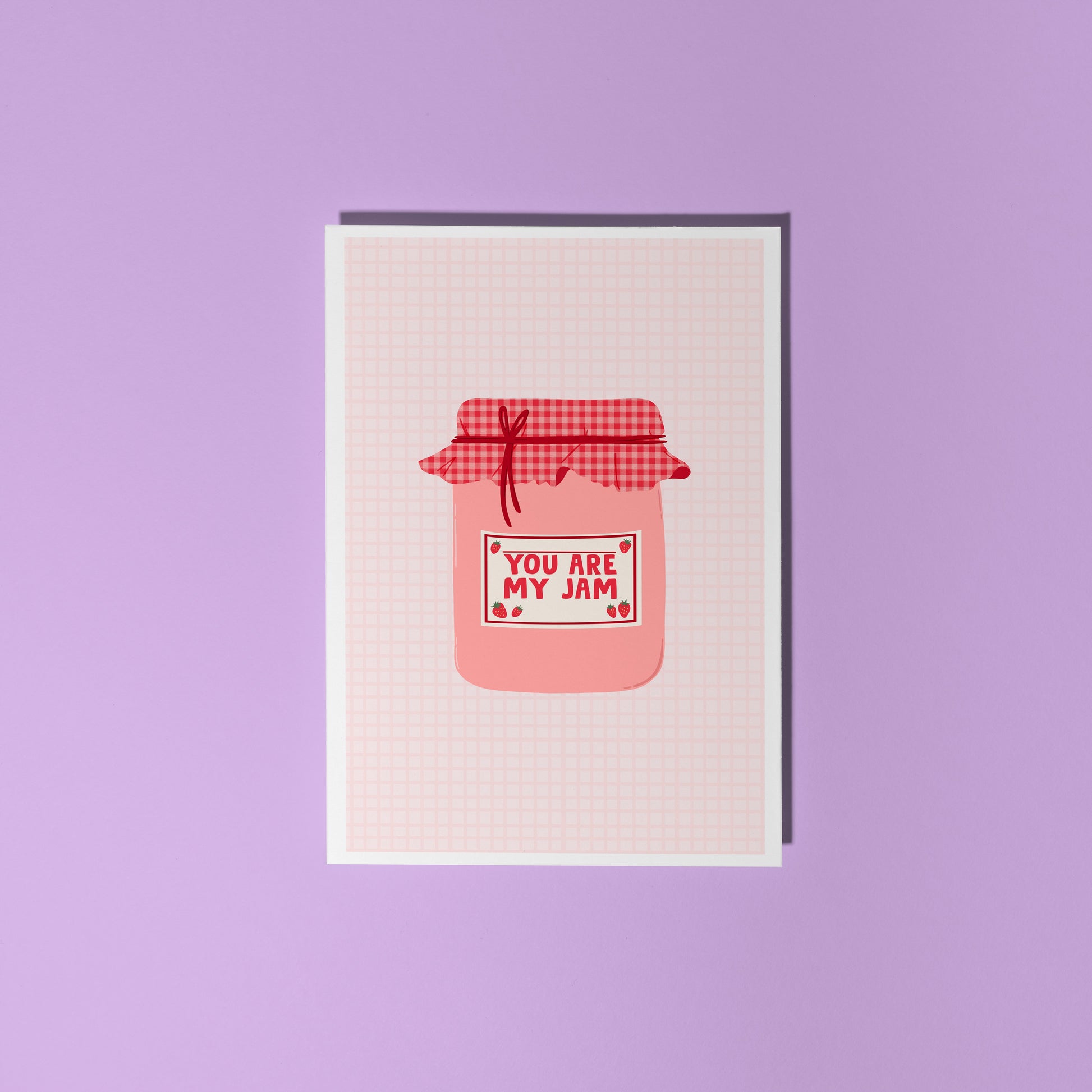 A greeting card with an illustration of a jam jar, with 'you are my jam' written on the label. The jam jar has a red and pink gingham lid and the label is decorated with strawberry doodles.