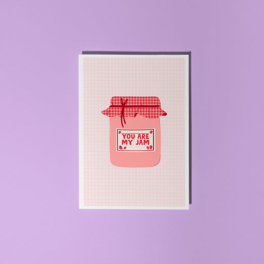 A greeting card with an illustration of a jam jar, with 'you are my jam' written on the label. The jam jar has a red and pink gingham lid and the label is decorated with strawberry doodles.