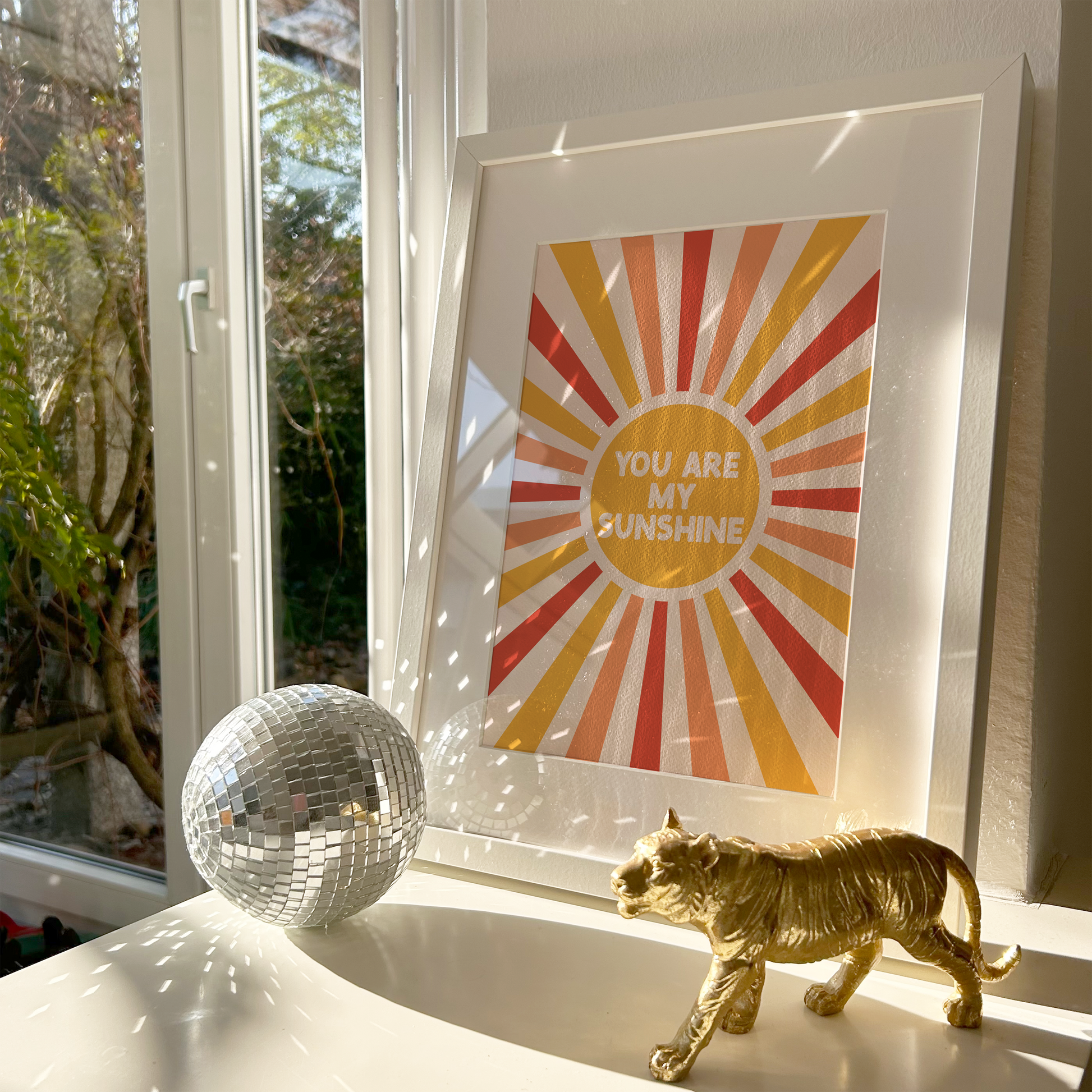 Framed print with 'You are my sunshine' text on a windowsill with decorative items.