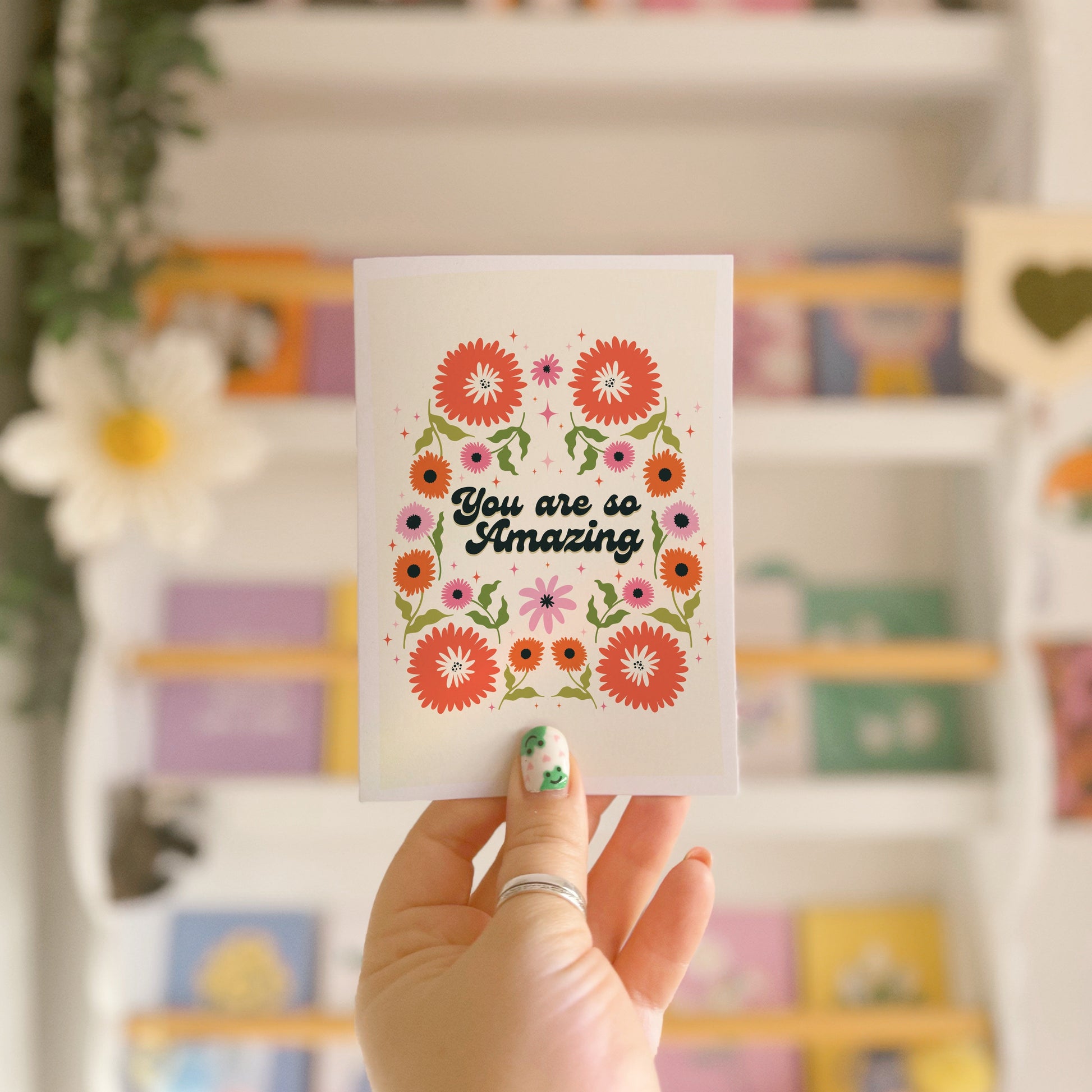 Hand holding a thank you card with 'You are so amazing' written on the front and floral detailing.