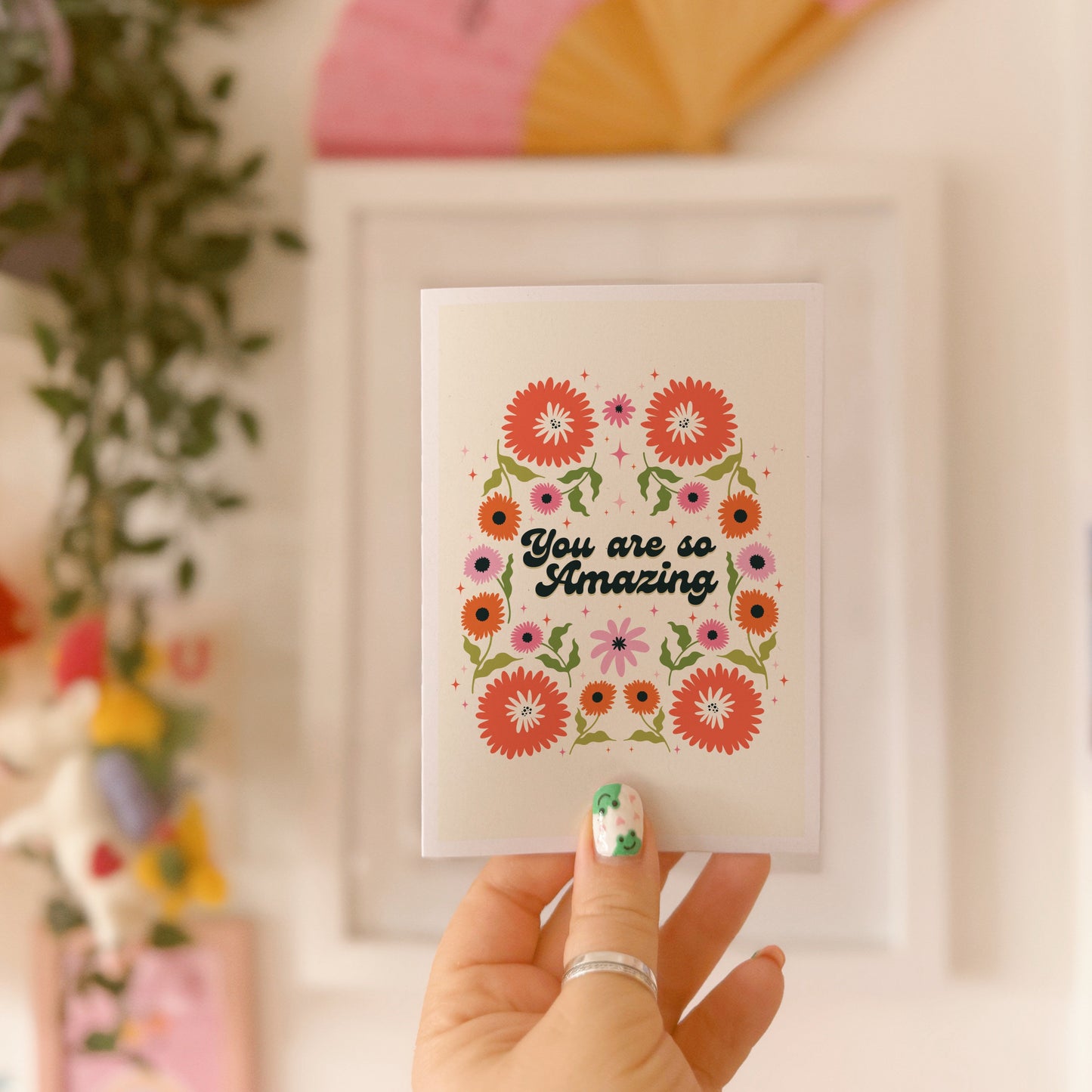 Hand holding a thank you card with 'You are so amazing' written on the front and floral detailing.