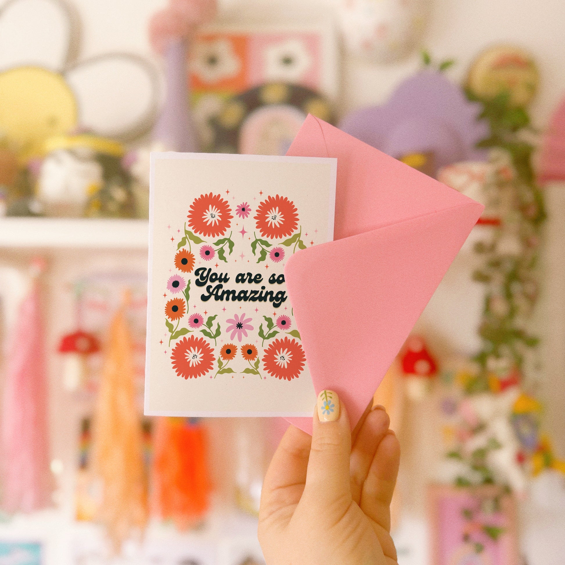 Hand holding a thank you card with 'You are so amazing' written on the front and floral detailing.