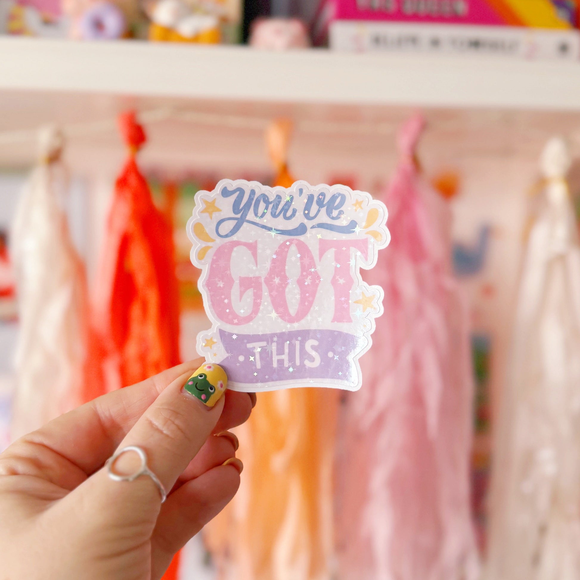 A holographic sticker with script writing saying 'you've got this' in blue, pink and purple, with little yellow illustrated detailing around the text.