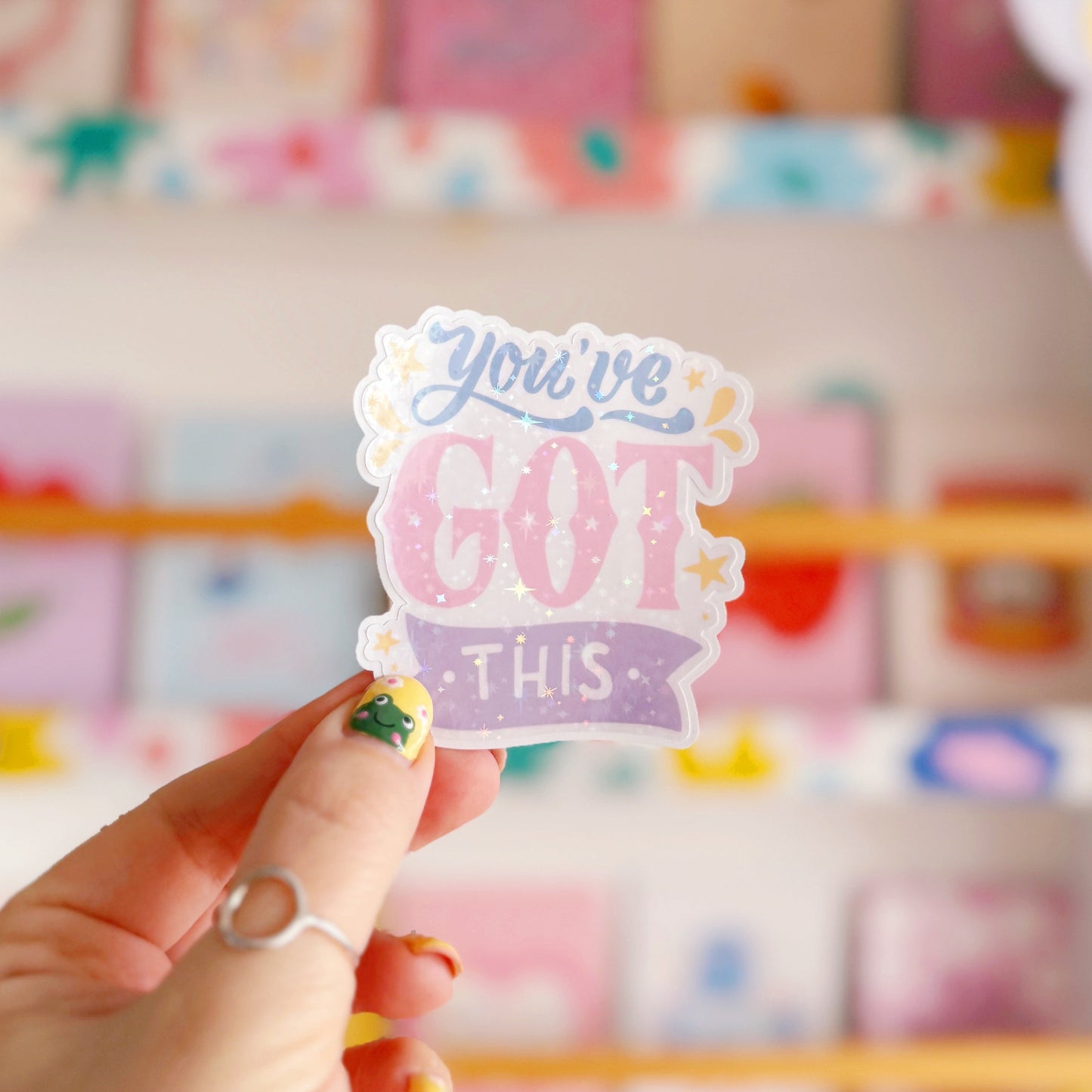 A holographic sticker with script writing saying 'you've got this' in blue, pink and purple, with little yellow illustrated detailing around the text.