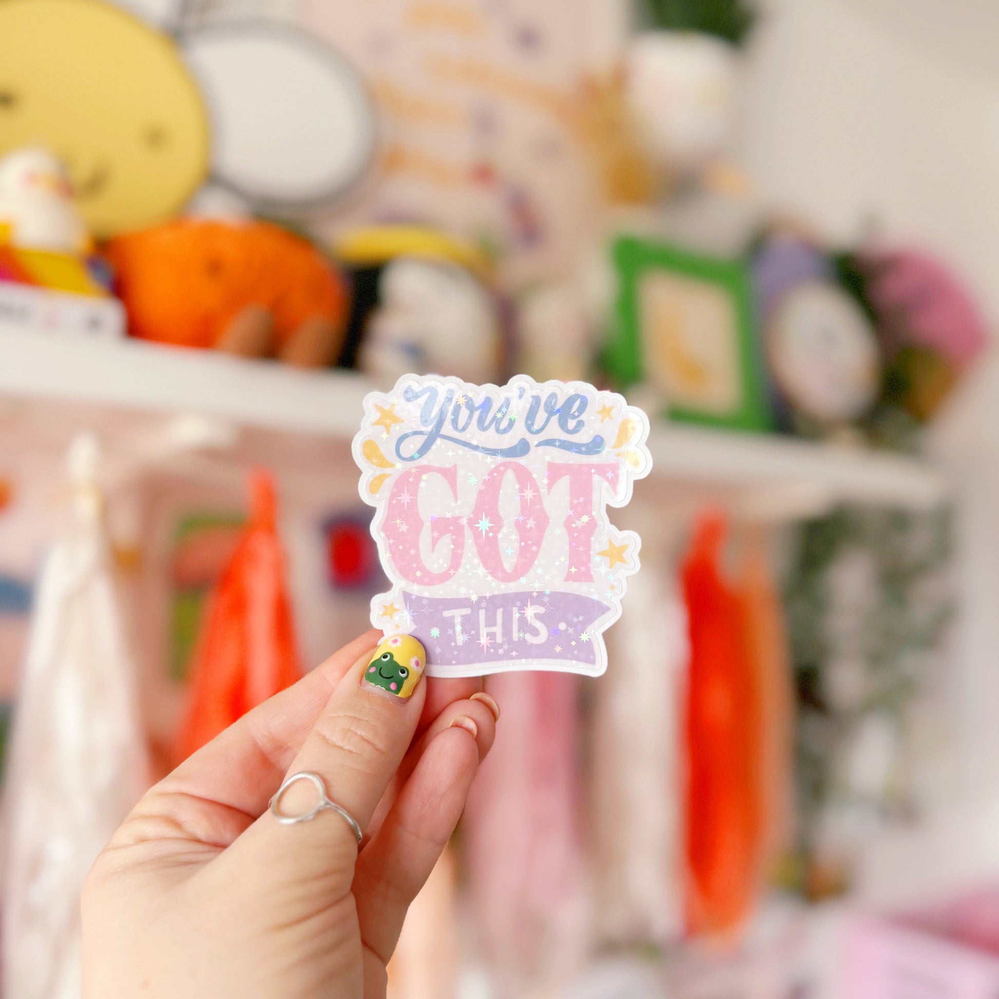 A holographic sticker with script writing saying 'you've got this' in blue, pink and purple, with little yellow illustrated detailing around the text.