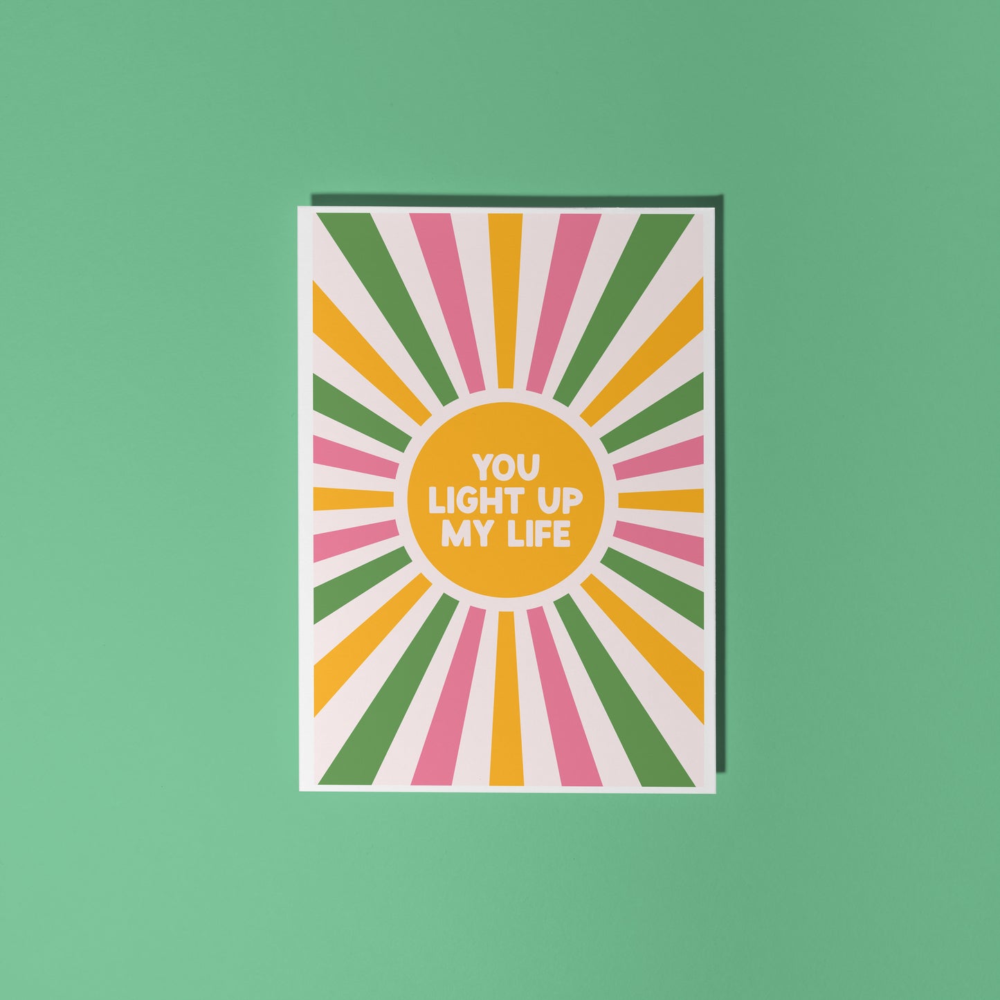 A pink, green and yellow star burst design with the words 'you light up my life' in the centre.