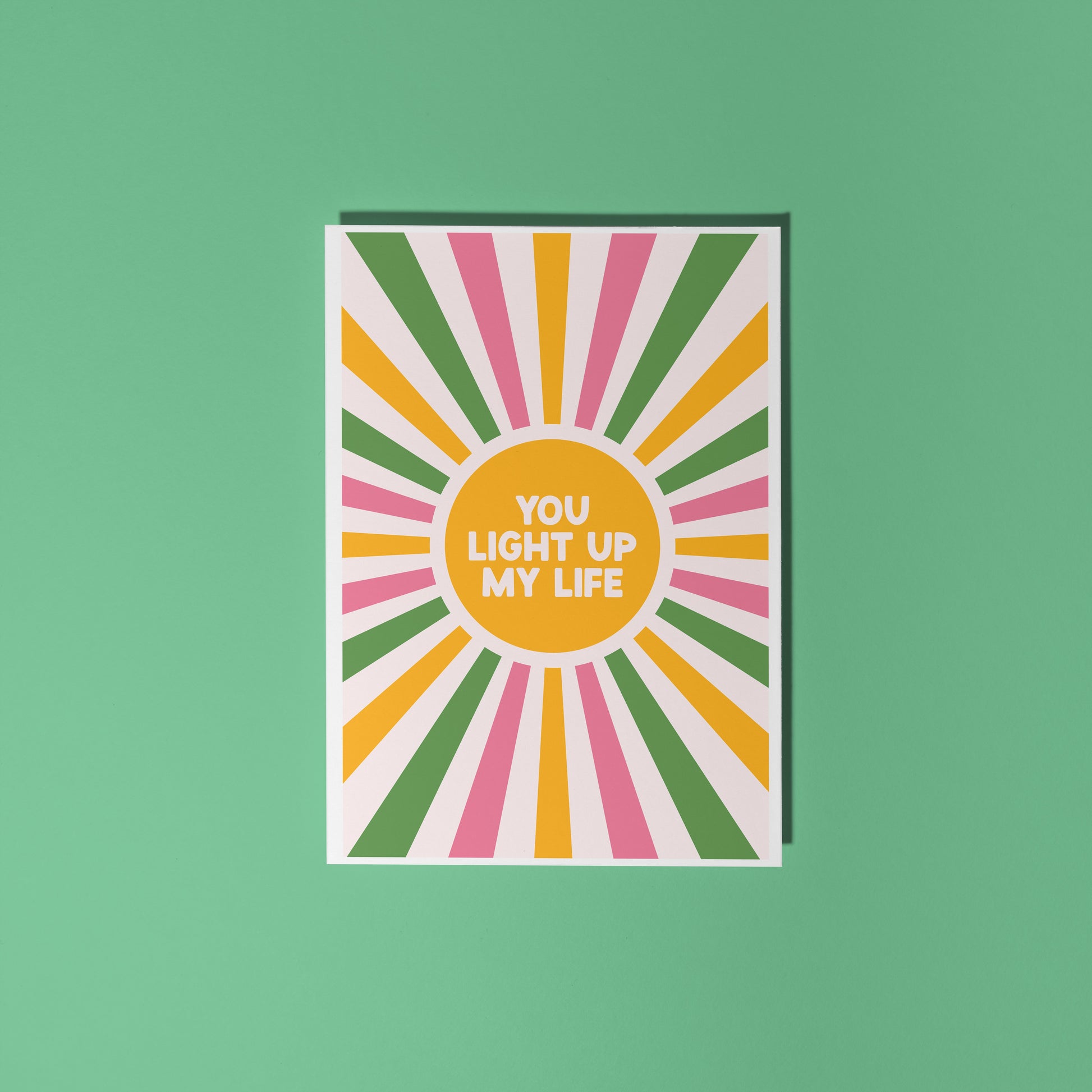 A pink, green and yellow star burst design with the words 'you light up my life' in the centre.