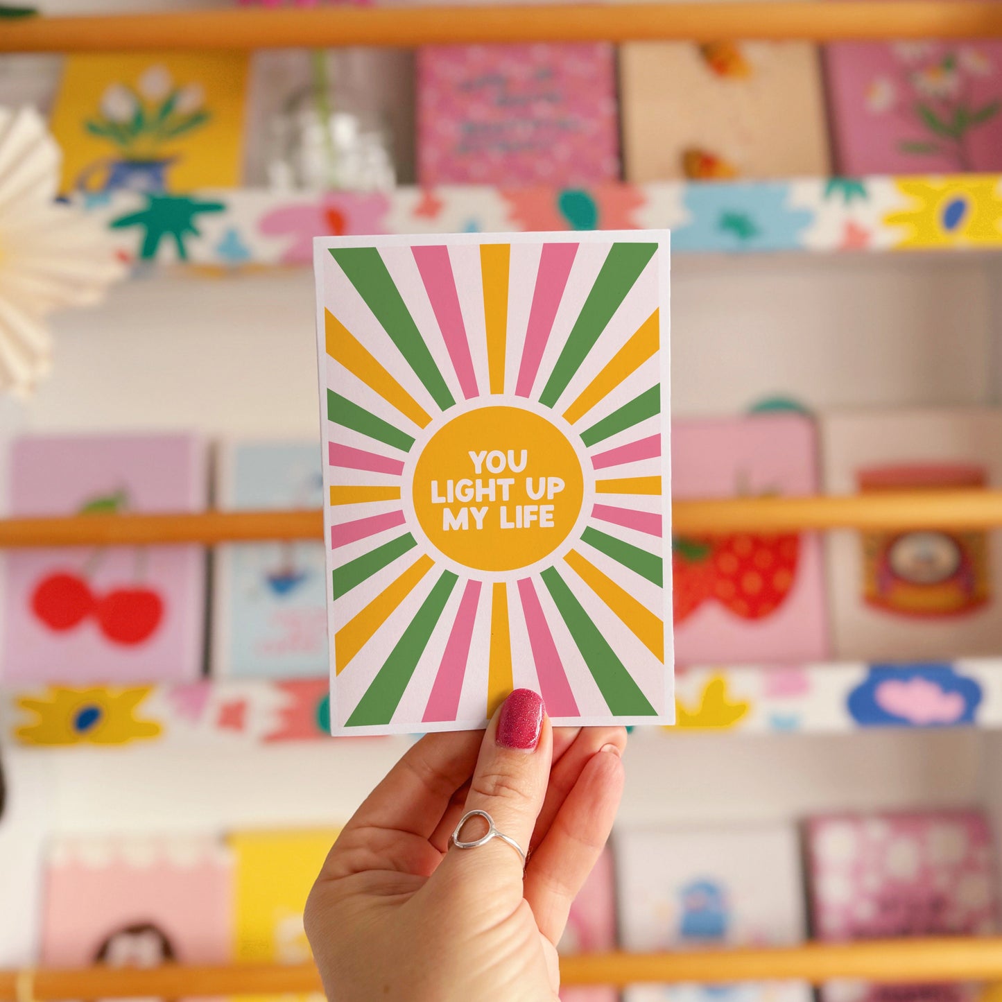 A pink, green and yellow star burst design with the words 'you light up my life' in the centre.