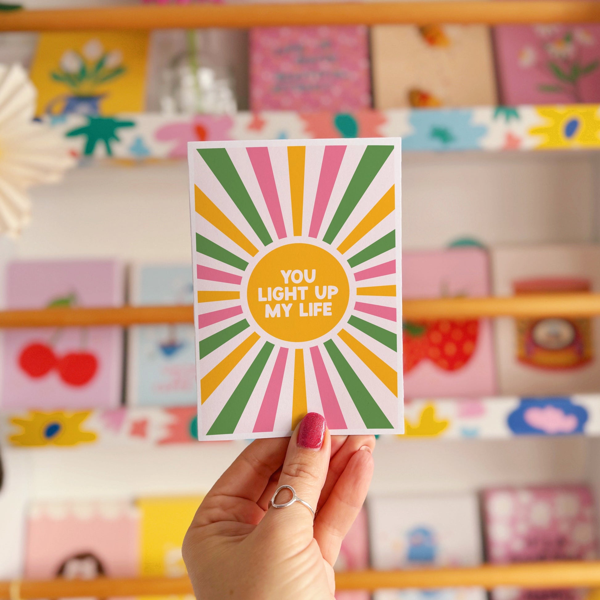 A pink, green and yellow star burst design with the words 'you light up my life' in the centre.