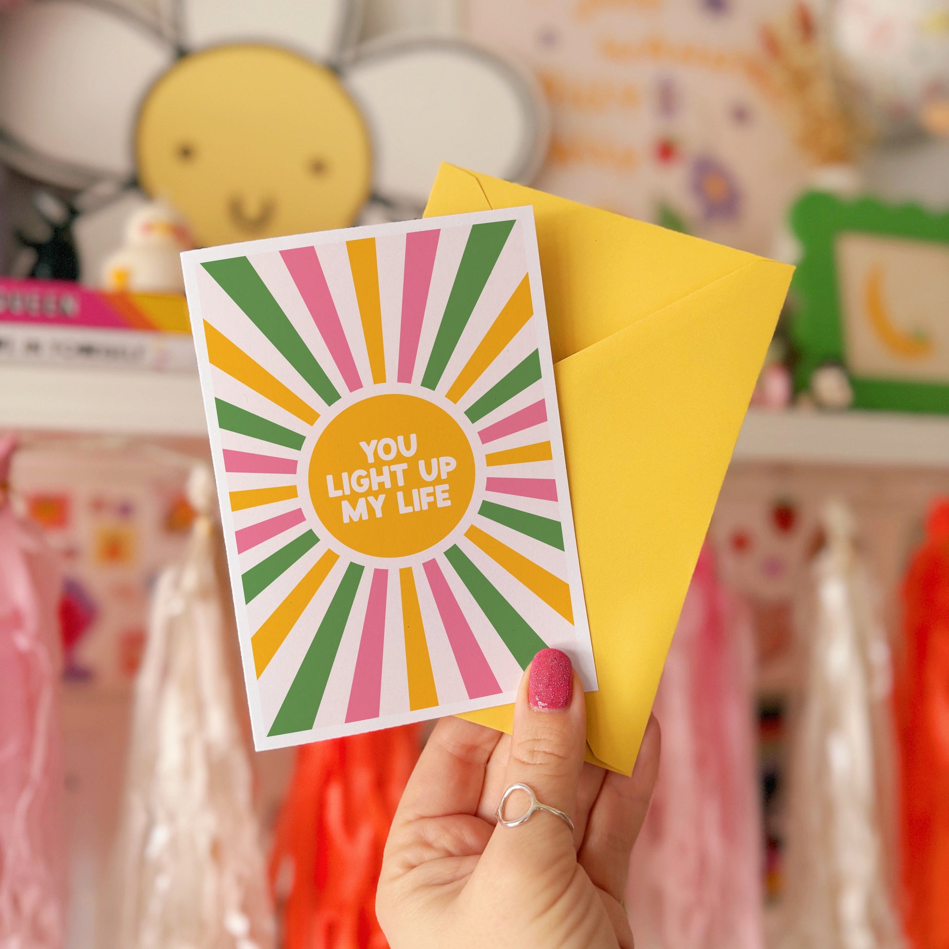 A pink, green and yellow star burst design with the words 'you light up my life' in the centre.