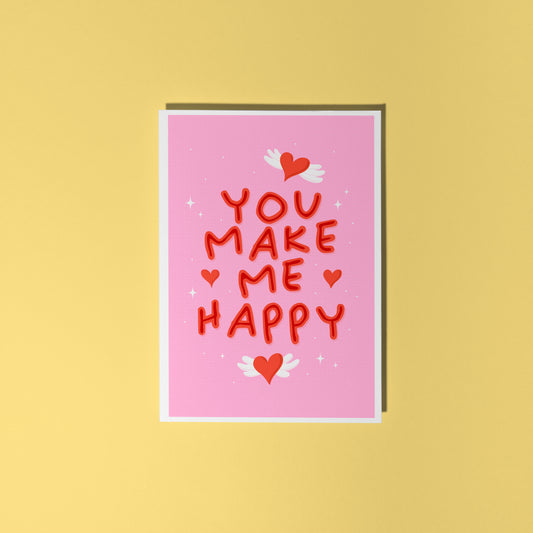 A pink greeting card with little heart illustrations around a red hand lettered quote that says 'you make me happy'.