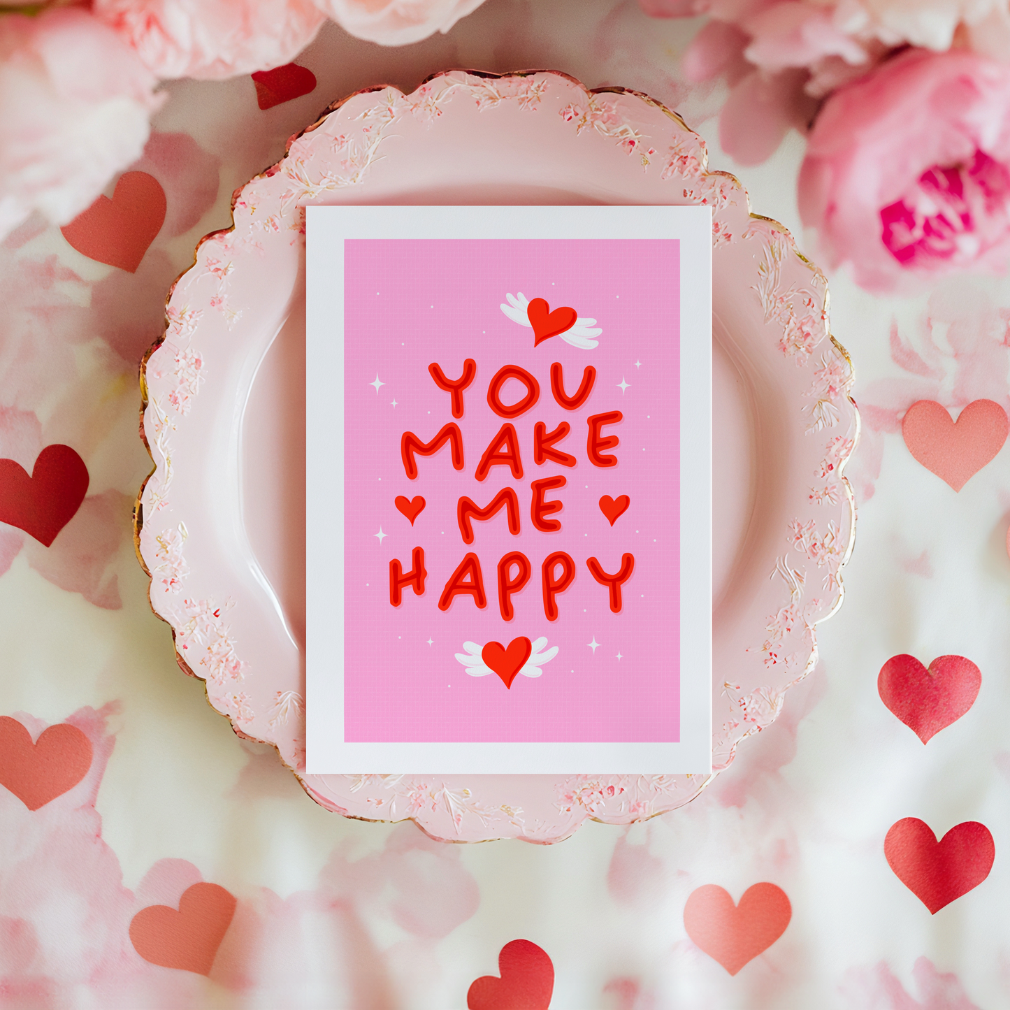 A pink greeting card with little heart illustrations around a red hand lettered quote that says 'you make me happy'.