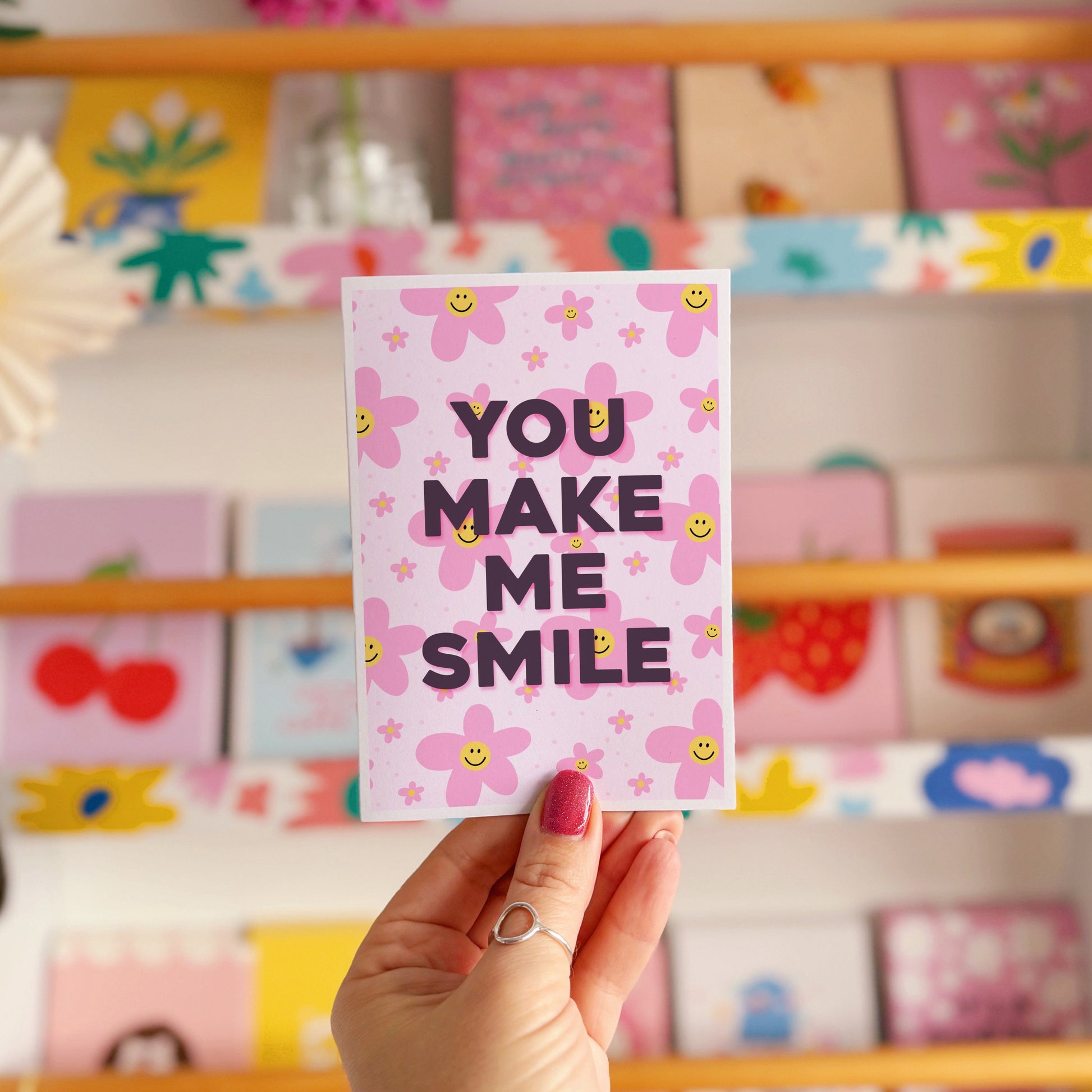 A pink card with smiling flowers, and tex that reads 'You make me smile.