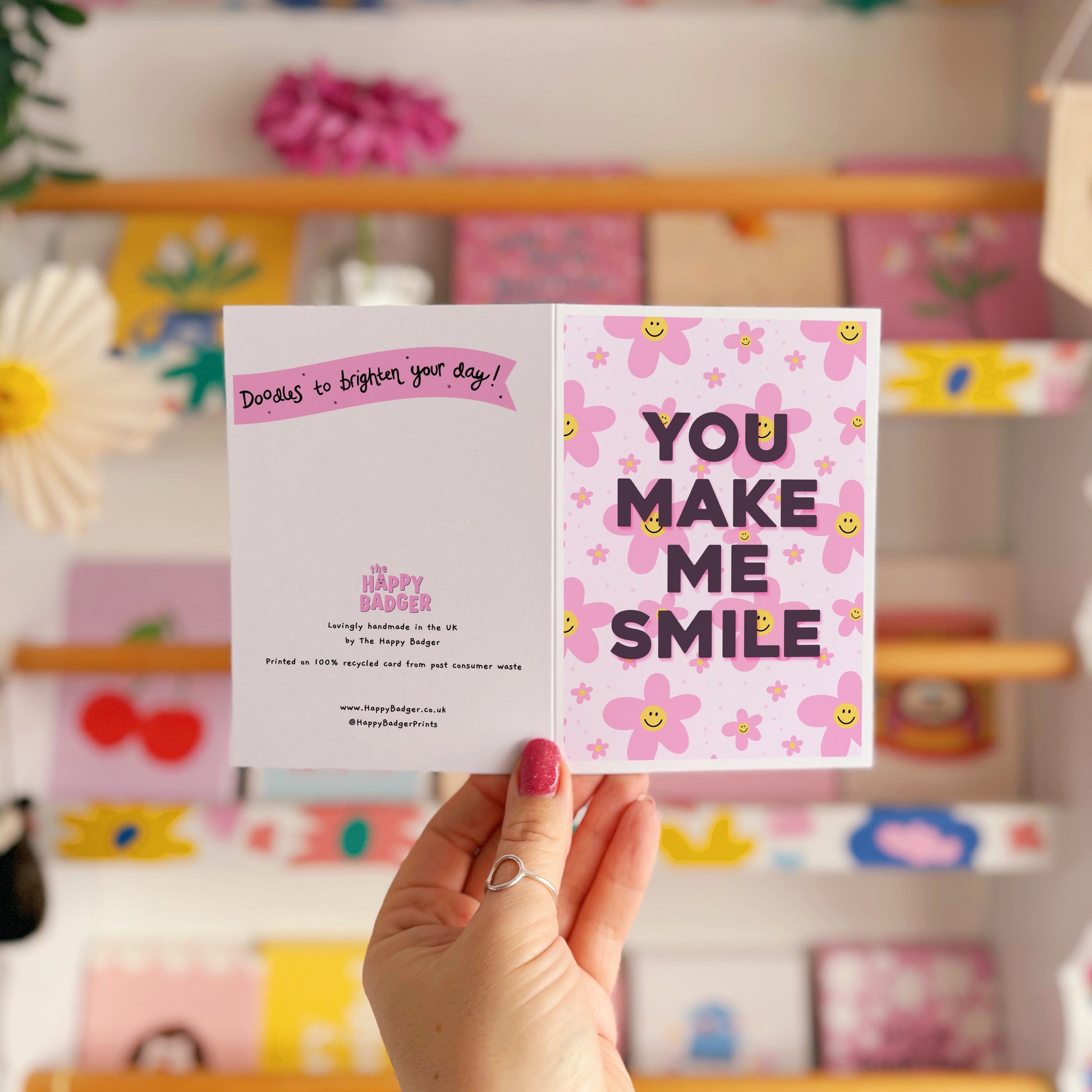 A pink card with smiling flowers, and tex that reads 'You make me smile.