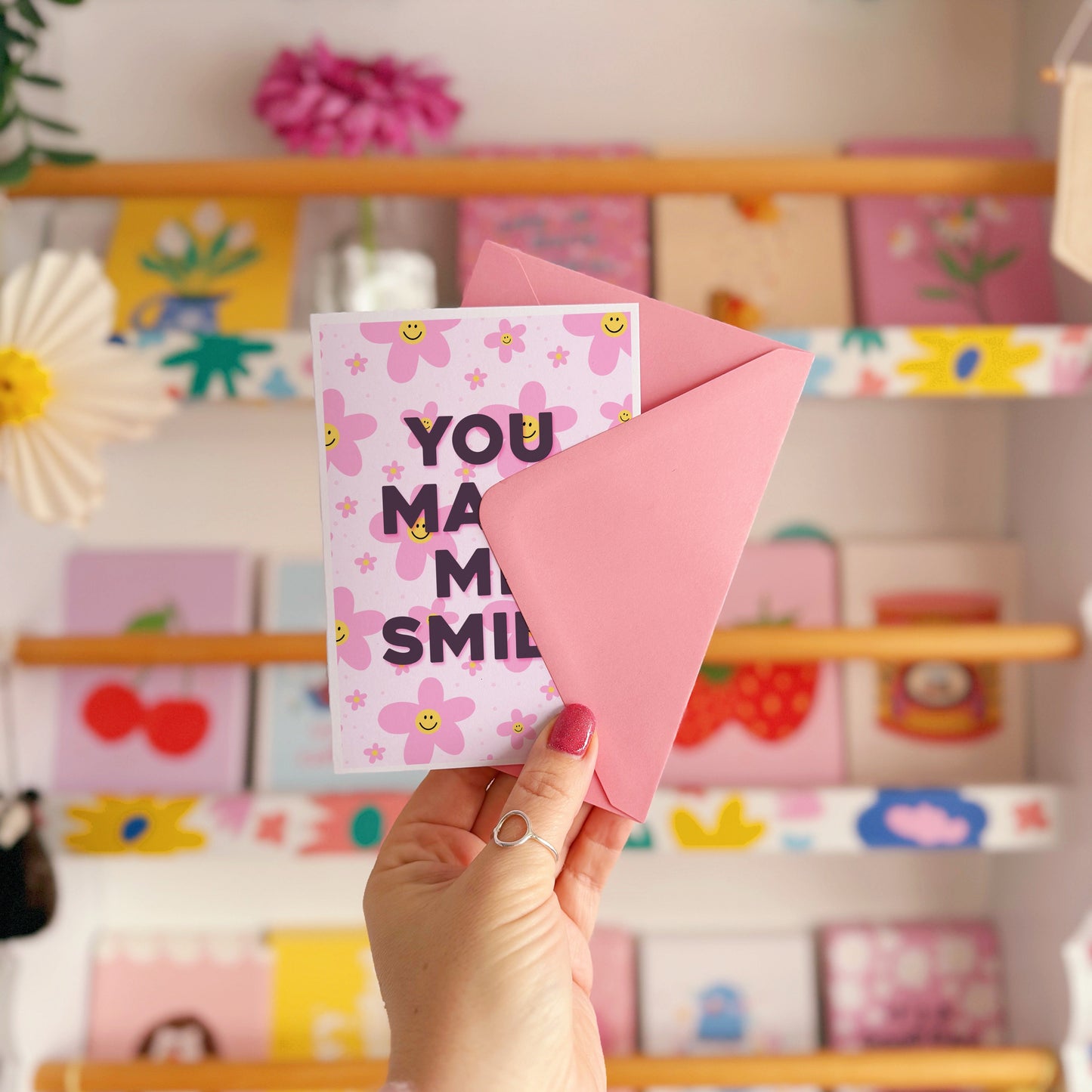 A pink card with smiling flowers, and tex that reads 'You make me smile.