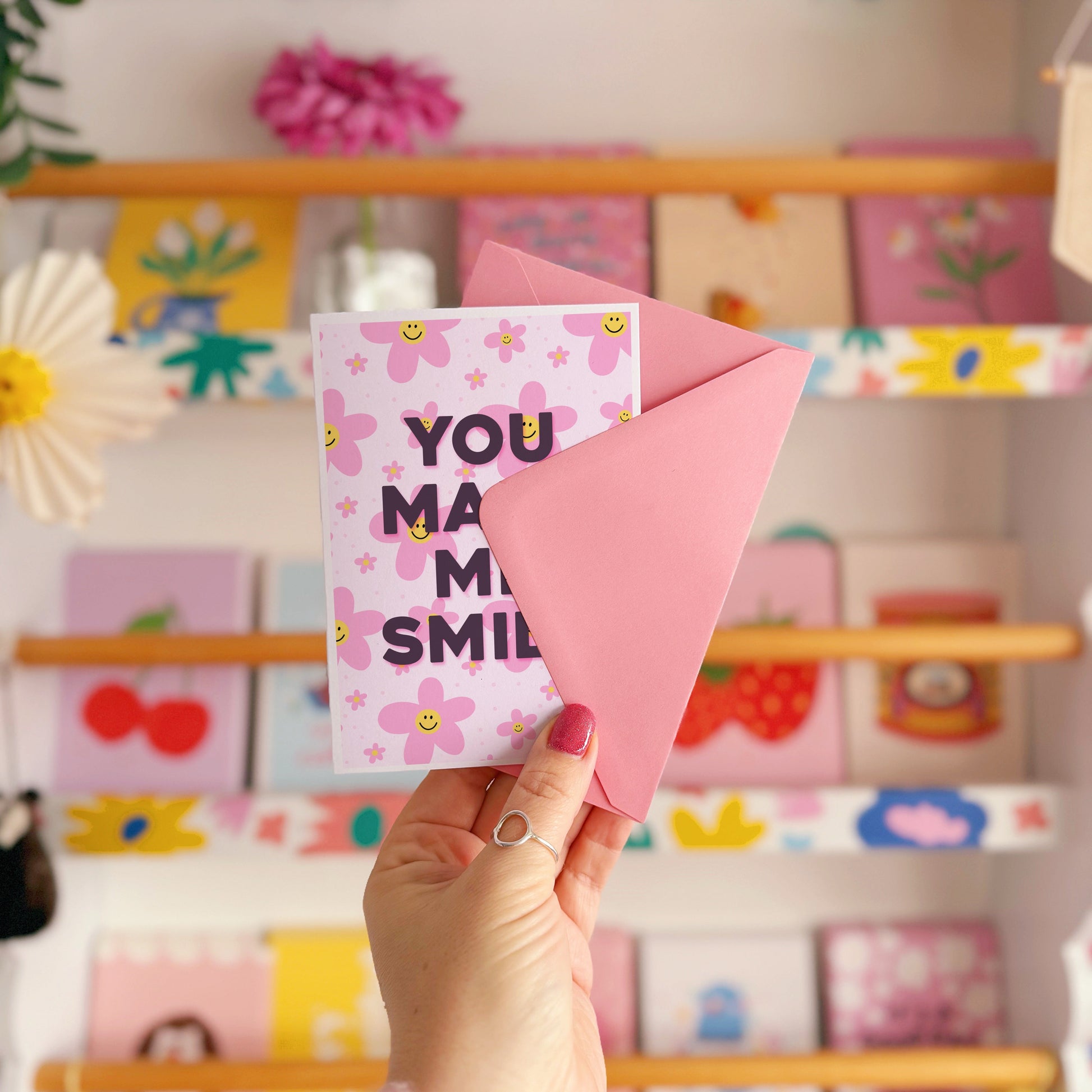 A pink card with smiling flowers, and tex that reads 'You make me smile.