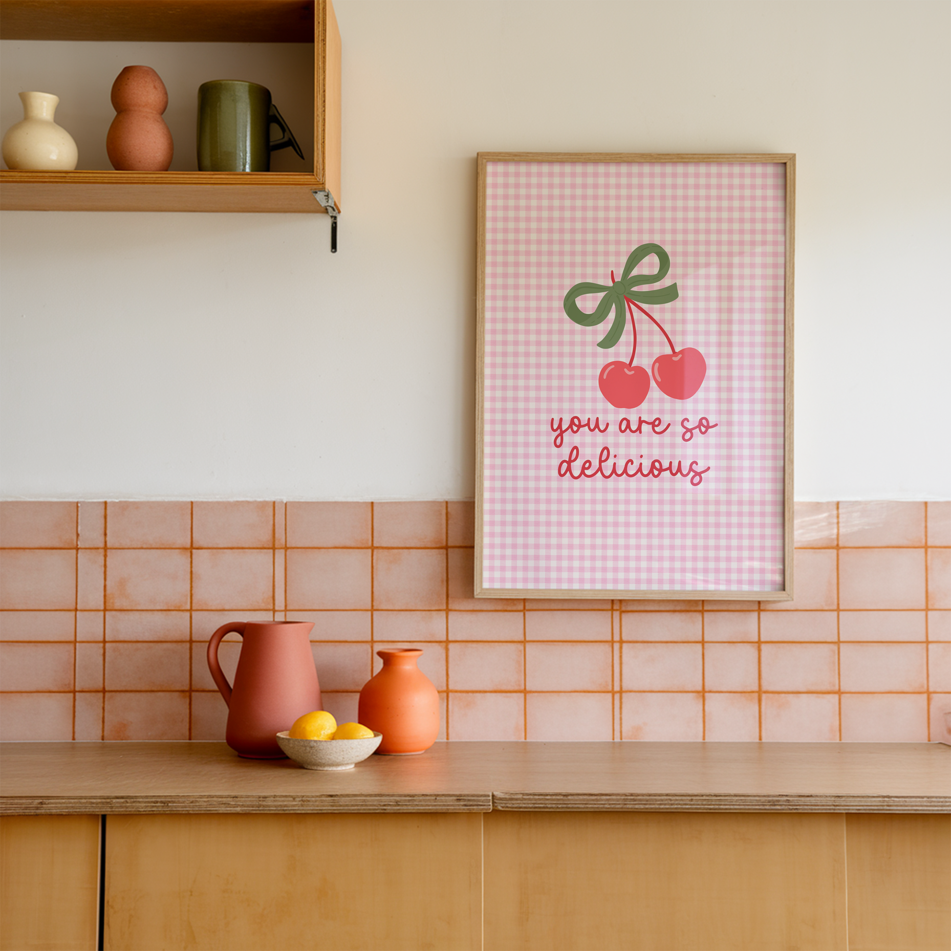 A pink gingham background print, with an illustration of red cherries tied together with a green bow, and the quote saying 'you are so delicious' below.