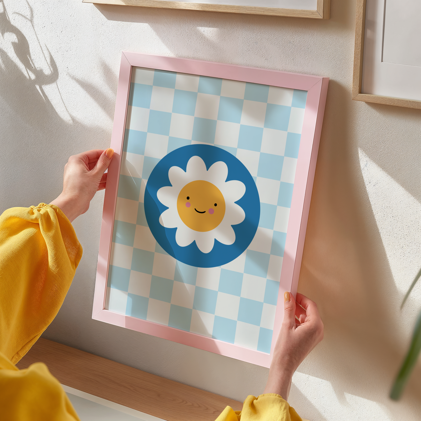 An illustration of a light blue checkerboard print, with a smiling daisy in a dark blue circle, shown in a frame.