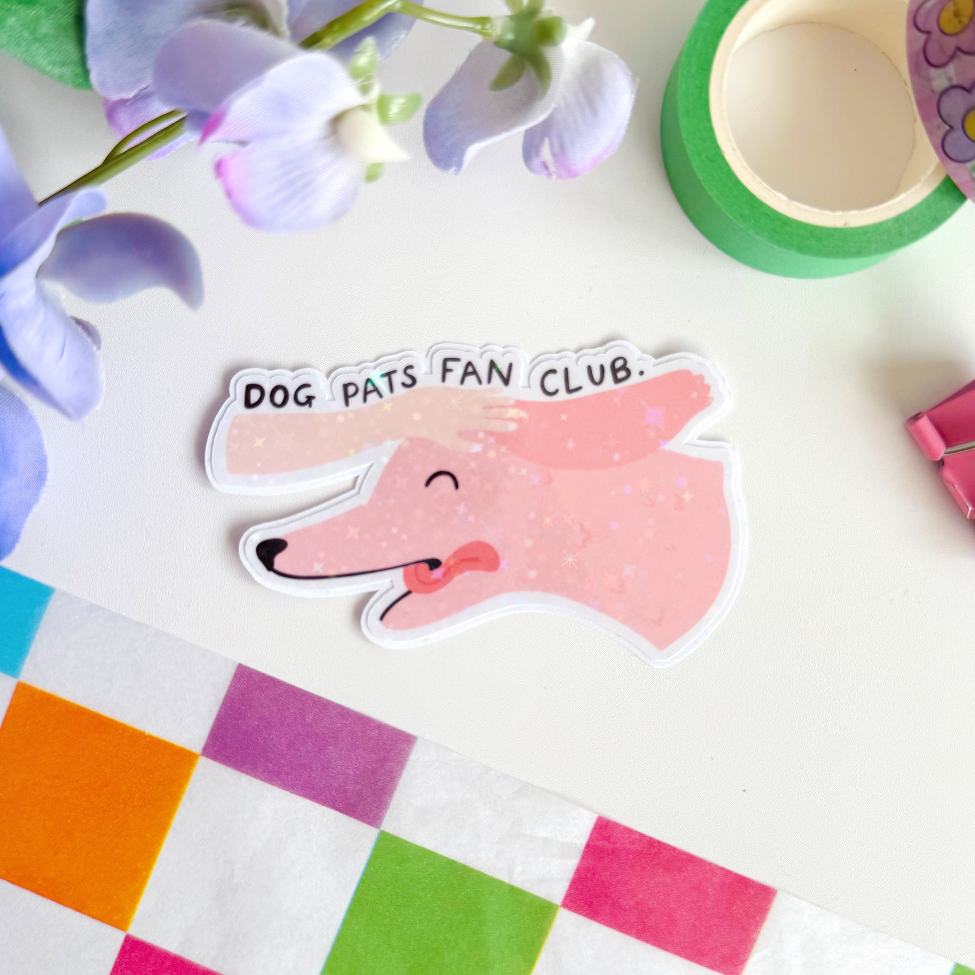 A holographic sticker of a pink dog, with its tongue sticking out, with a hand patting its head. The text reads 'Dog Pats Fan Club.'