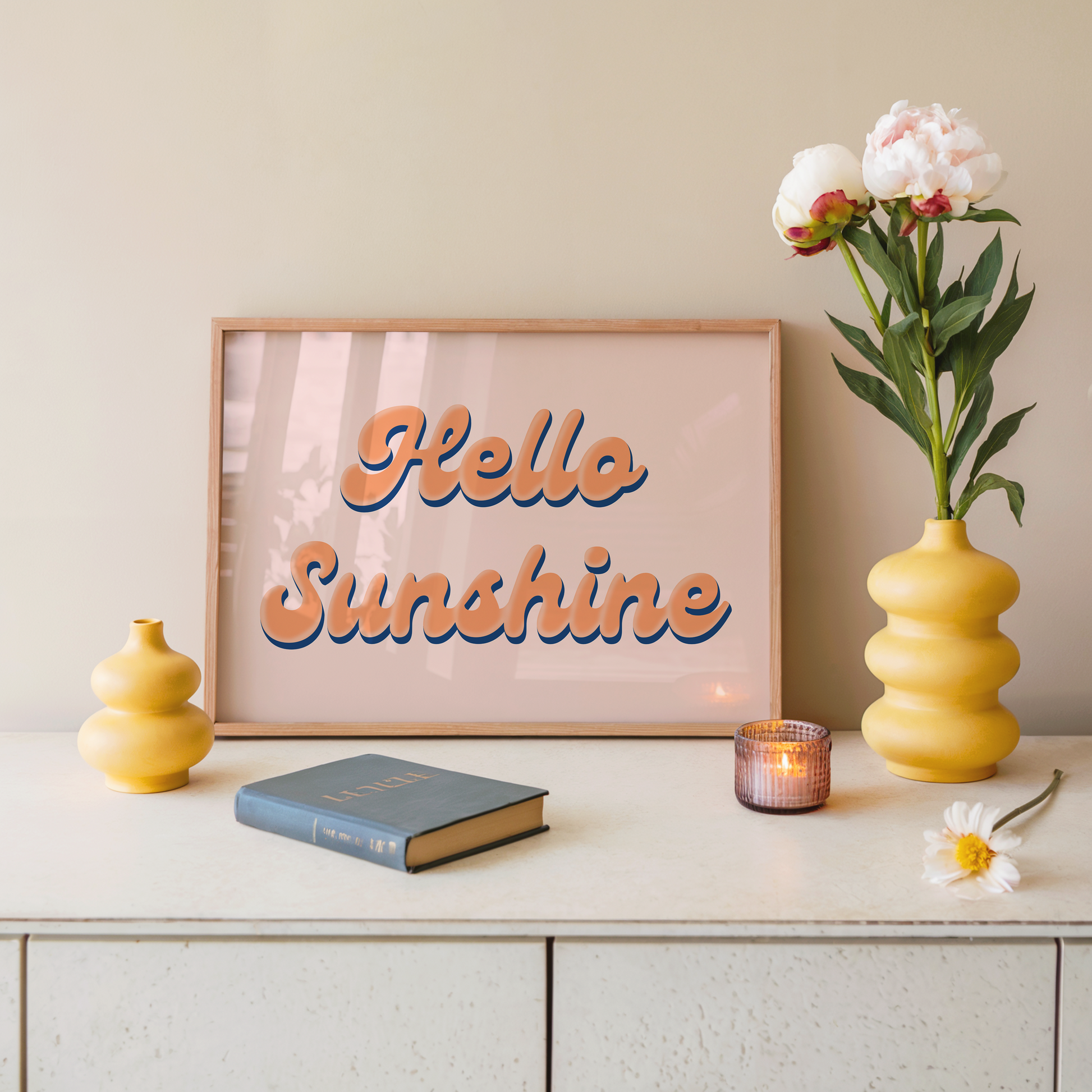 Decorative setup with 'Hello Sunshine' art print, books, candles, and flowers on a shelf.