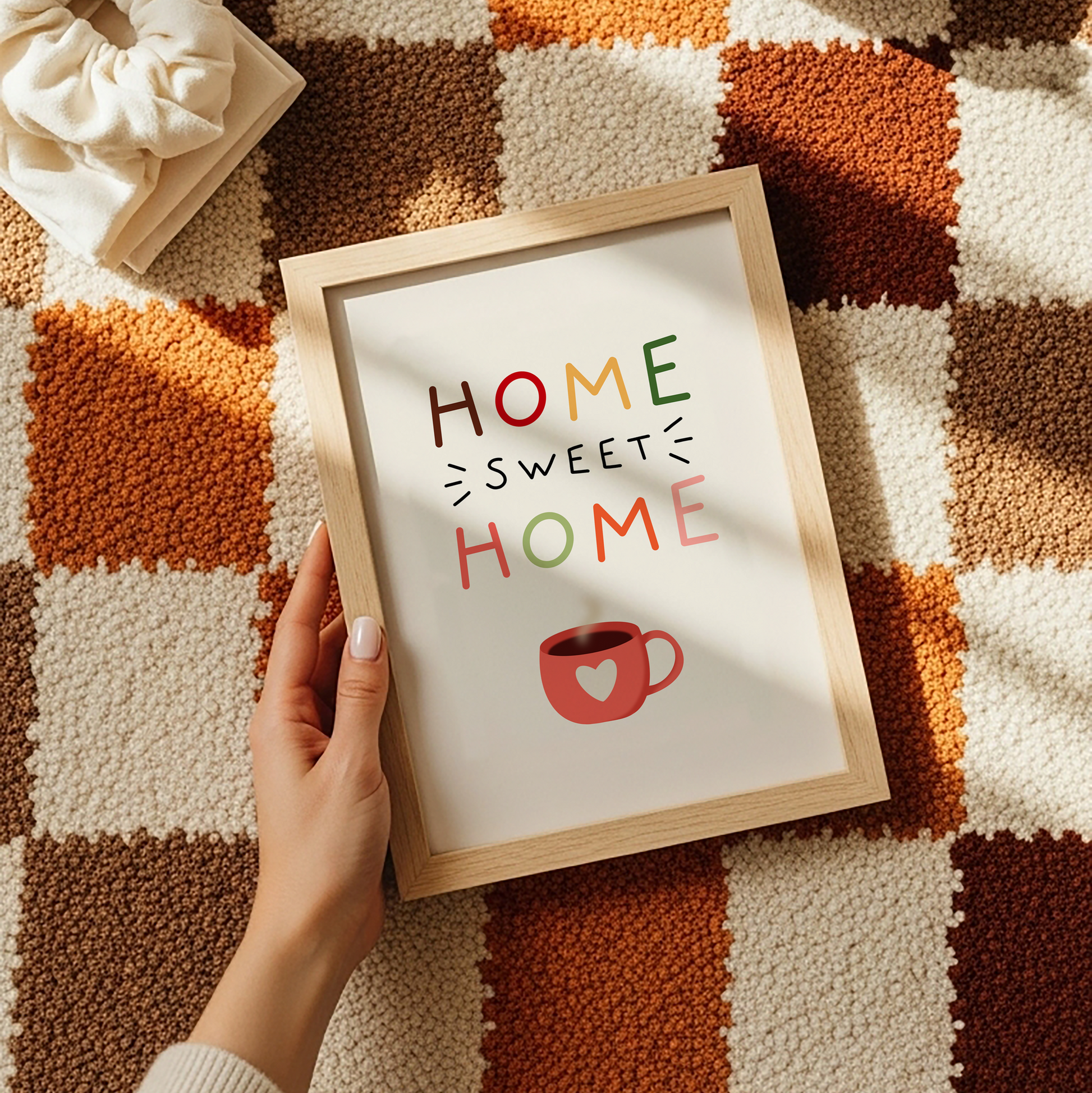 Framed 'Home Sweet Home' sign held by a hand on a checkered surface with a cup of coffee.