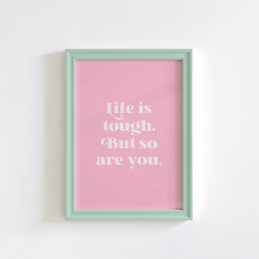 A framed print with a pink background and green frame, containing the text 'Life is tough. But so are you.' in a white font.