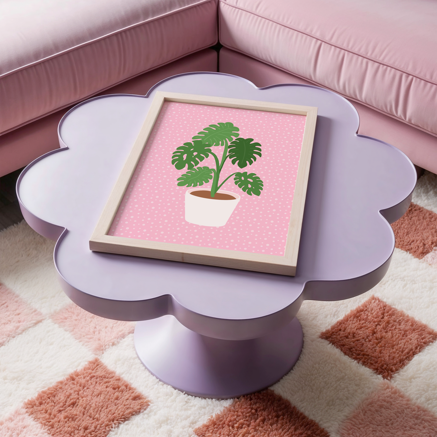 A framed print of a Monstera plant in a pot, with green leaves on a pink background.