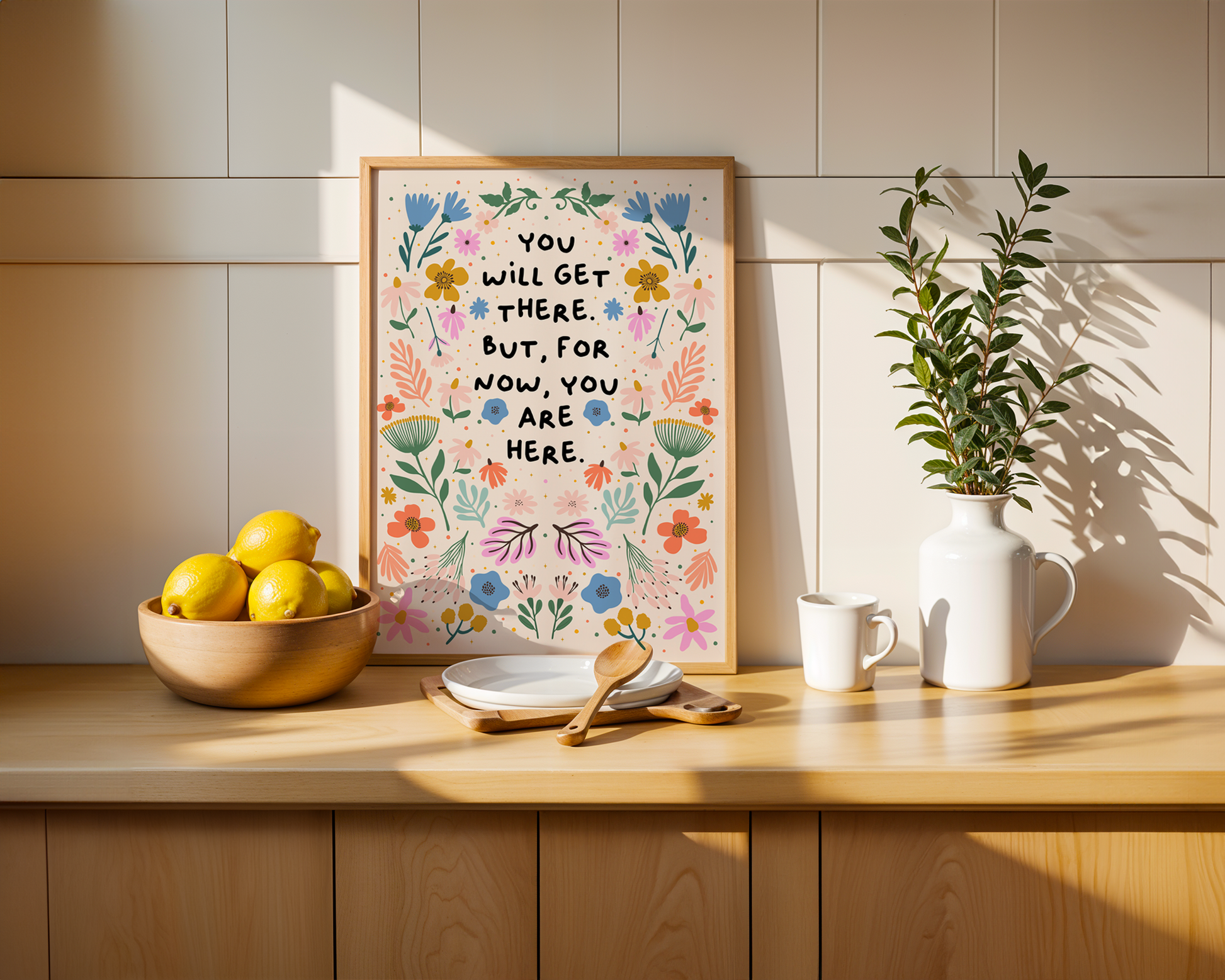 A floral illustration print, drawn in a symmetrical pattern with vibrant blues, oranges and greens and pinks - surrounding a quote in black handwriting that says you will get there. but for now, you are here.