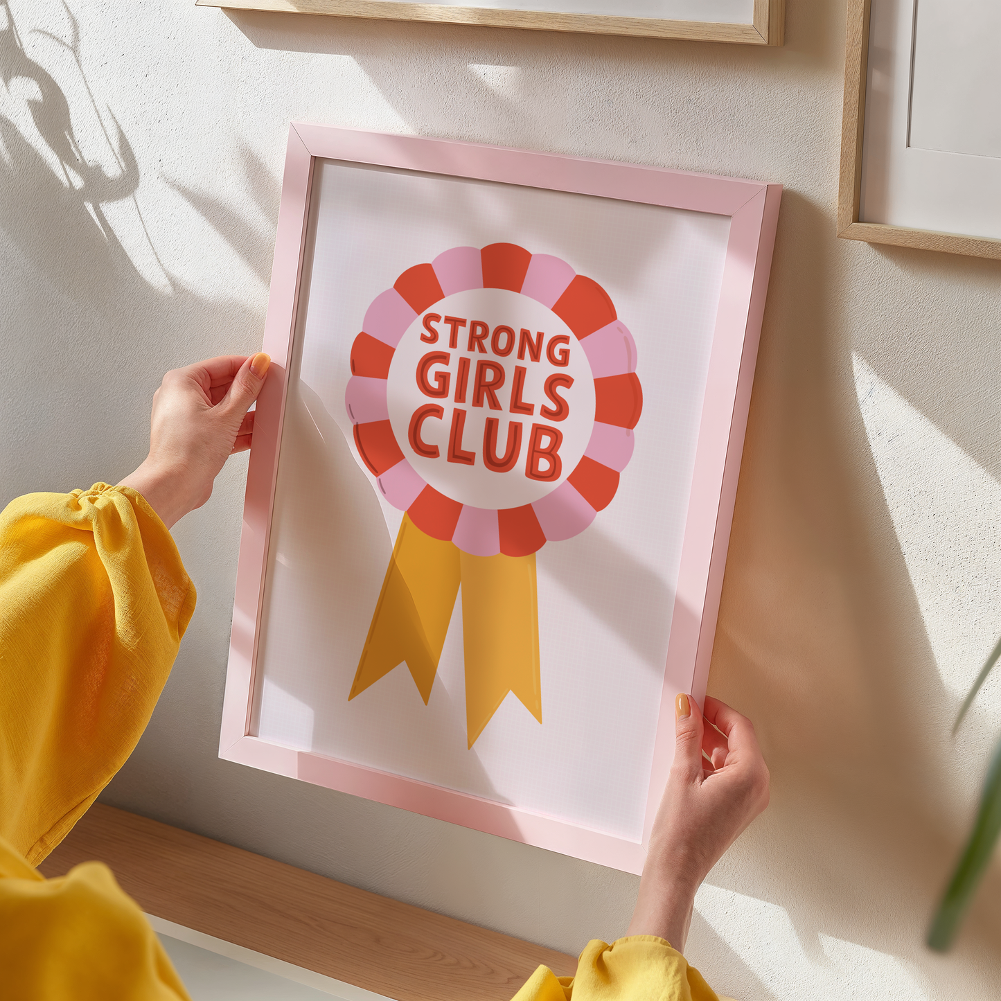An illustration of a rosette style award, in red, pink and yellow. The award has the words 'Strong Girls Club' written in the centre of the rosette.