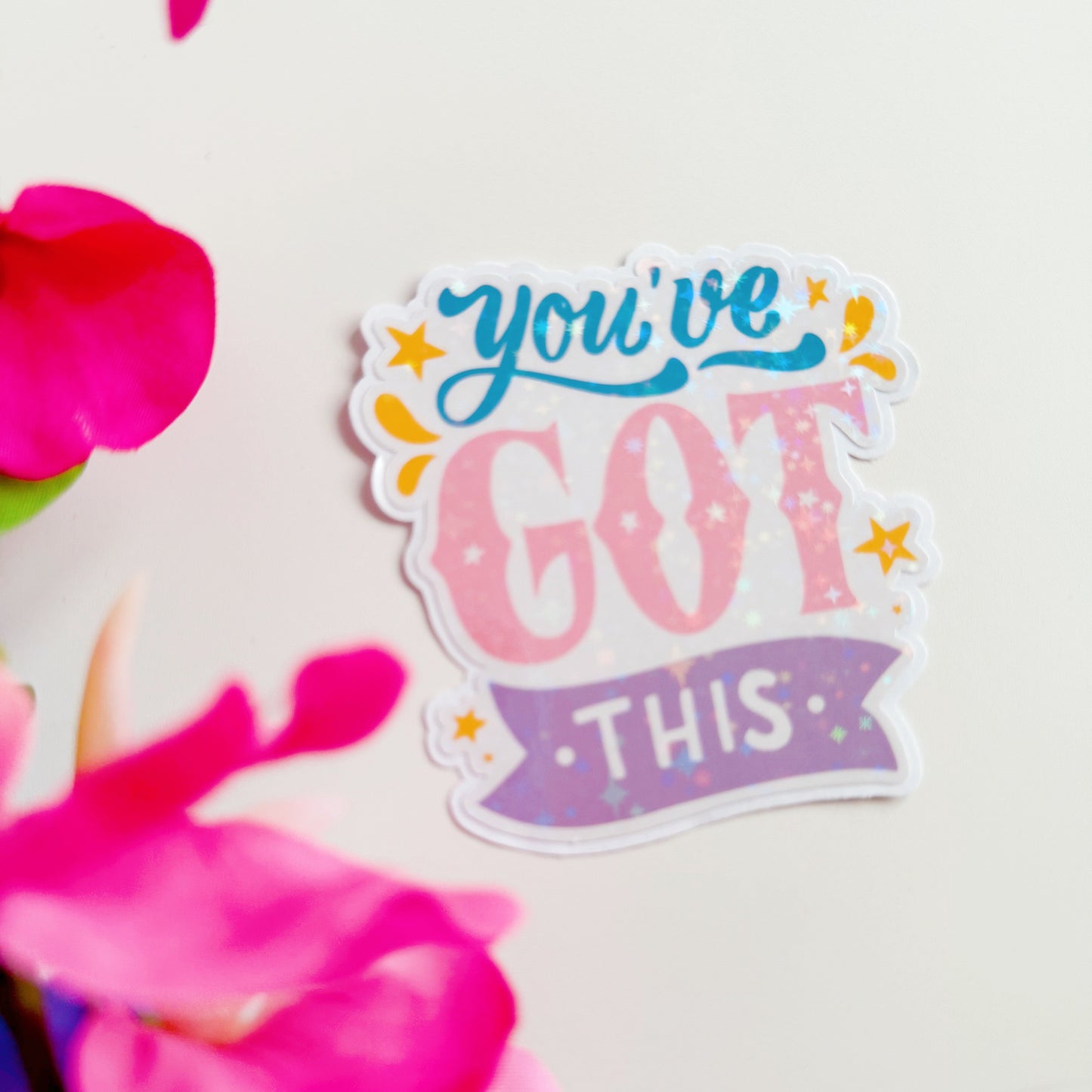 A holographic sticker, that says 'You've Got This' in pink blue and purple colours.