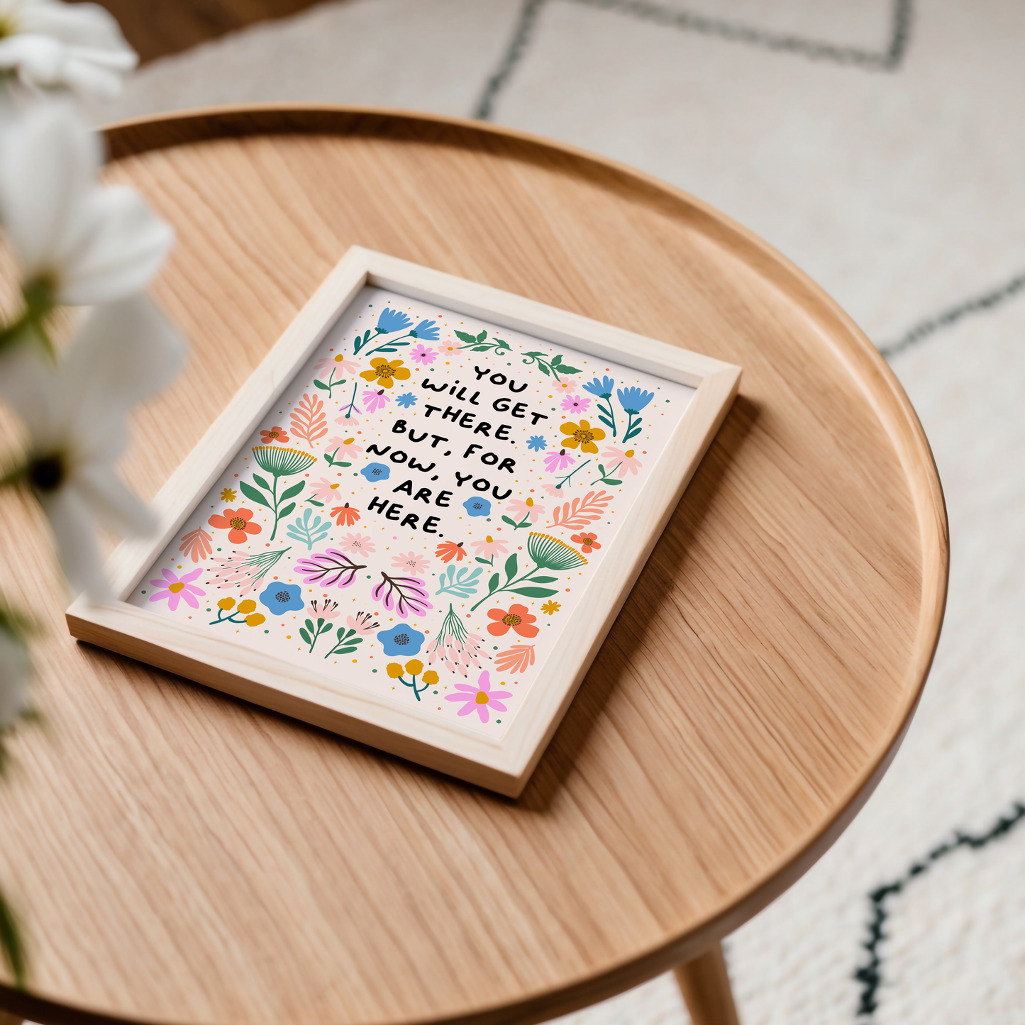 A floral illustration print, drawn in a symmetrical pattern with vibrant blues, oranges and greens and pinks - surrounding a quote in black handwriting that says you will get there. but for now, you are here.