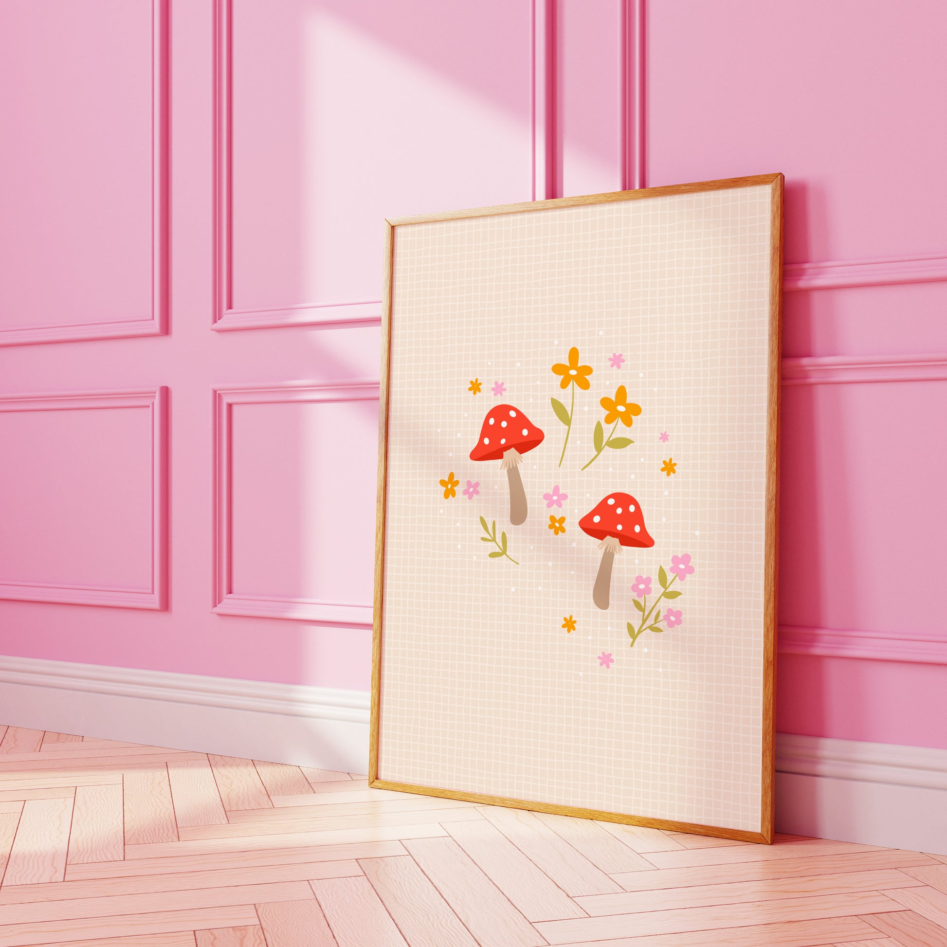 An illustration of a two cute mushrooms in shades of red and pink, surrounded by floral illustrations, shown in a frame against a pink wall.